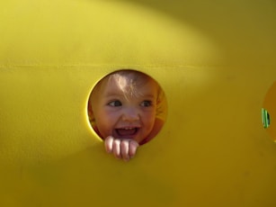 A little boy sticking his head out of a hole in a yellow wall