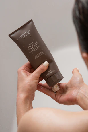 A woman holding a tube of cream in front of her face