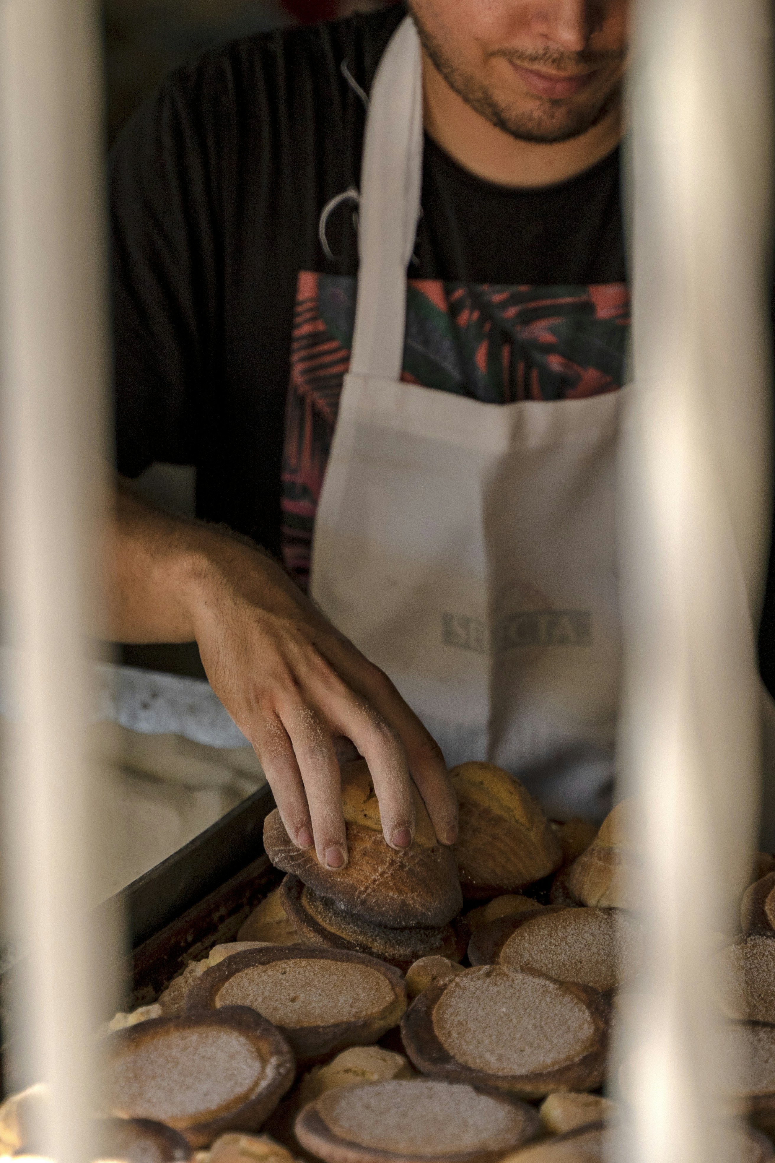 A man in an apron is putting some bread on a tray