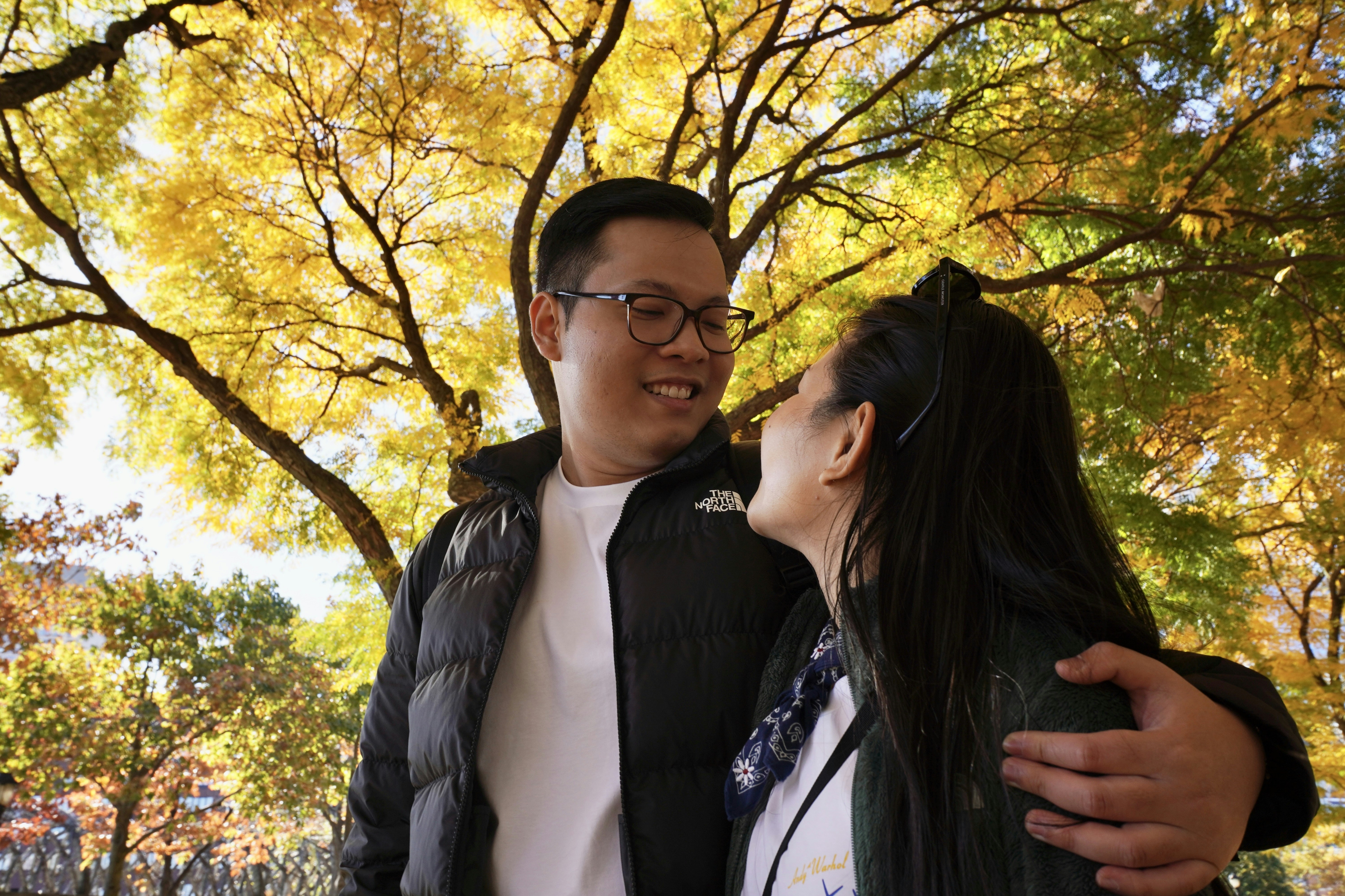 Vietnamese American couple sharing warm moment under golden autumn leaves