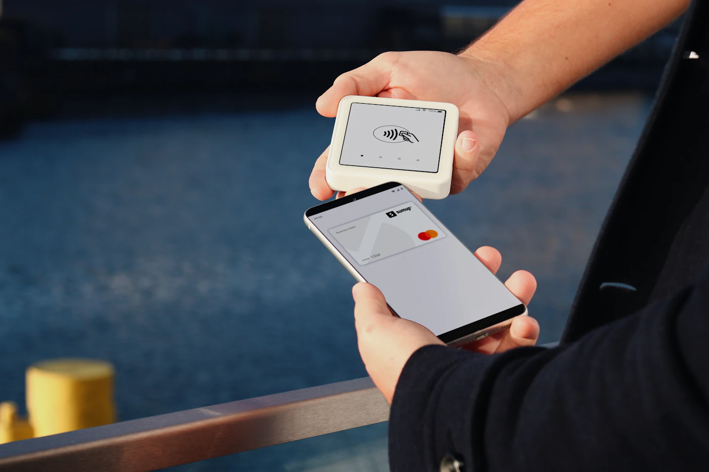 A hand holds a smartphone against a portable contactless card reader