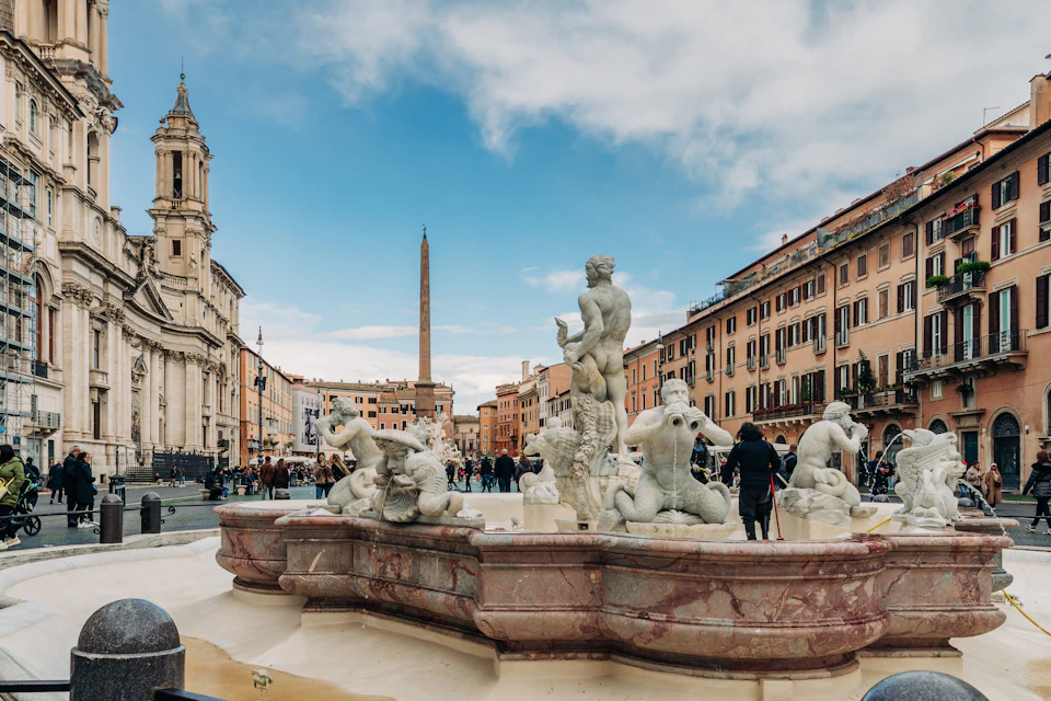Piazza Navona in winter sun, the Fontana del Moro in the foreground, the church of Sant'Agnese in Agone on the left and the obelisk of the Four Rivers fountain behind, with people in winter coats
