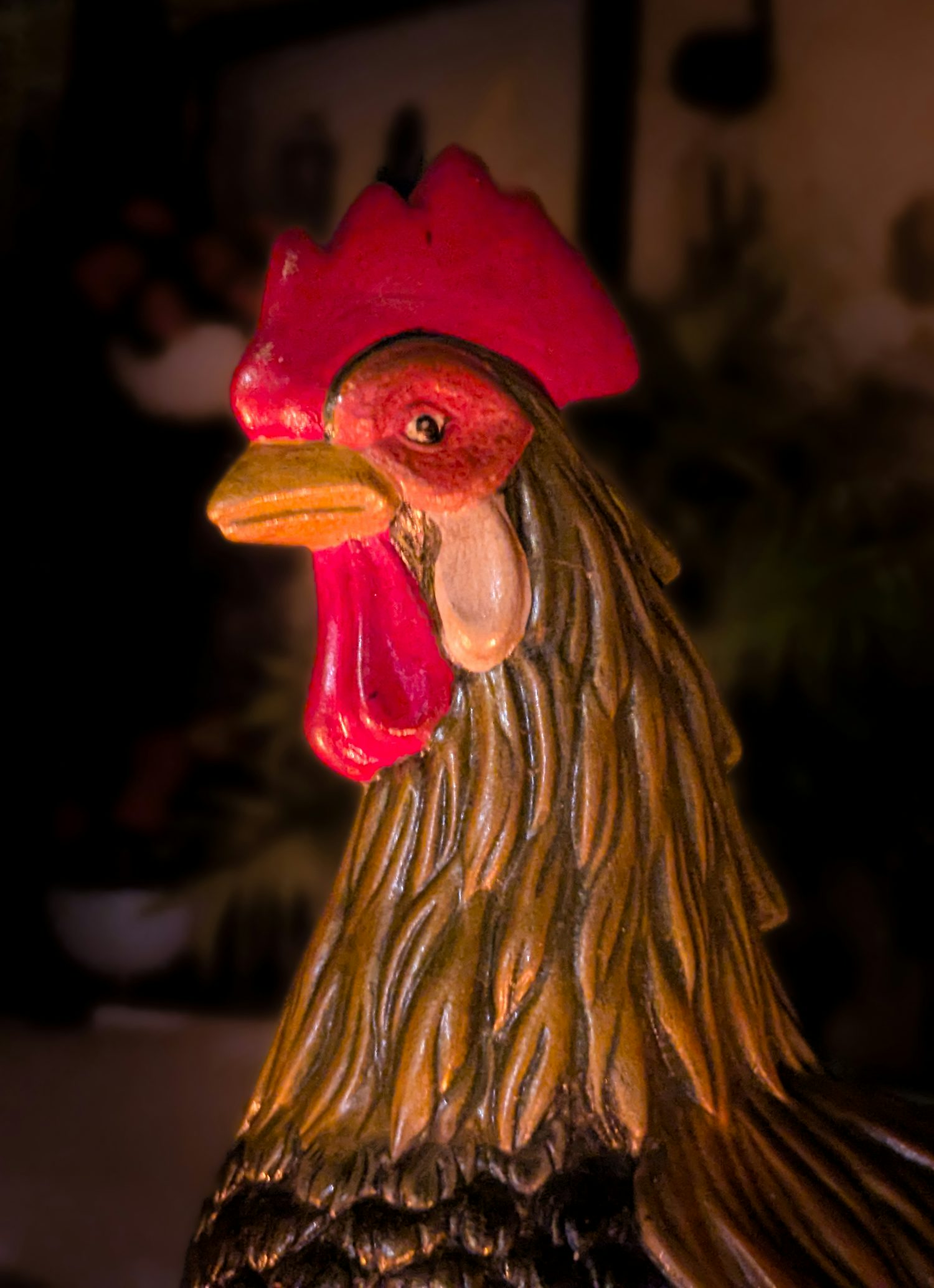 A close-up of a porcelain rooster bathed in candle light. The rooster has brown feathers, red comb, and yellow beak.