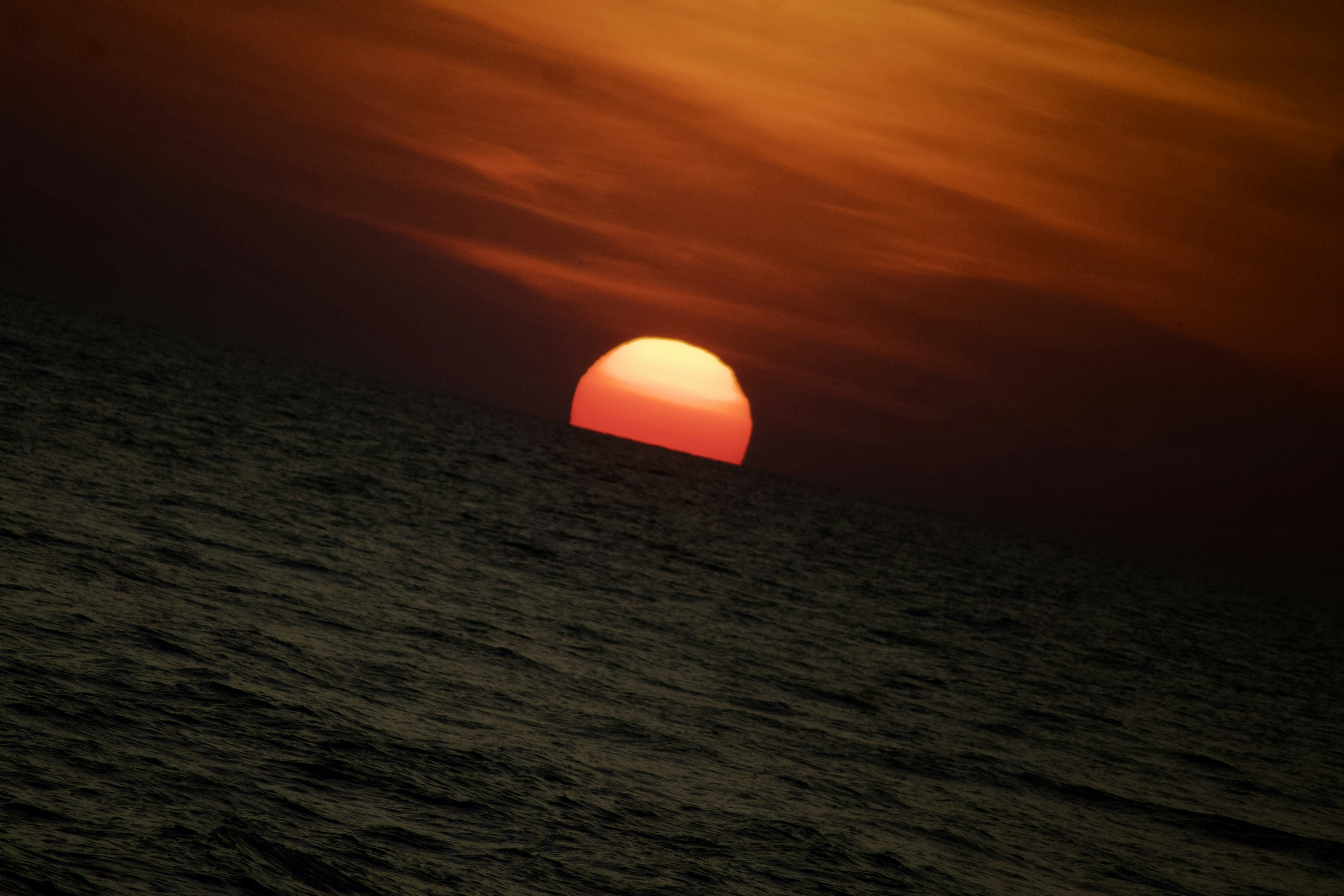 The sun is setting over the ocean on a cloudy day