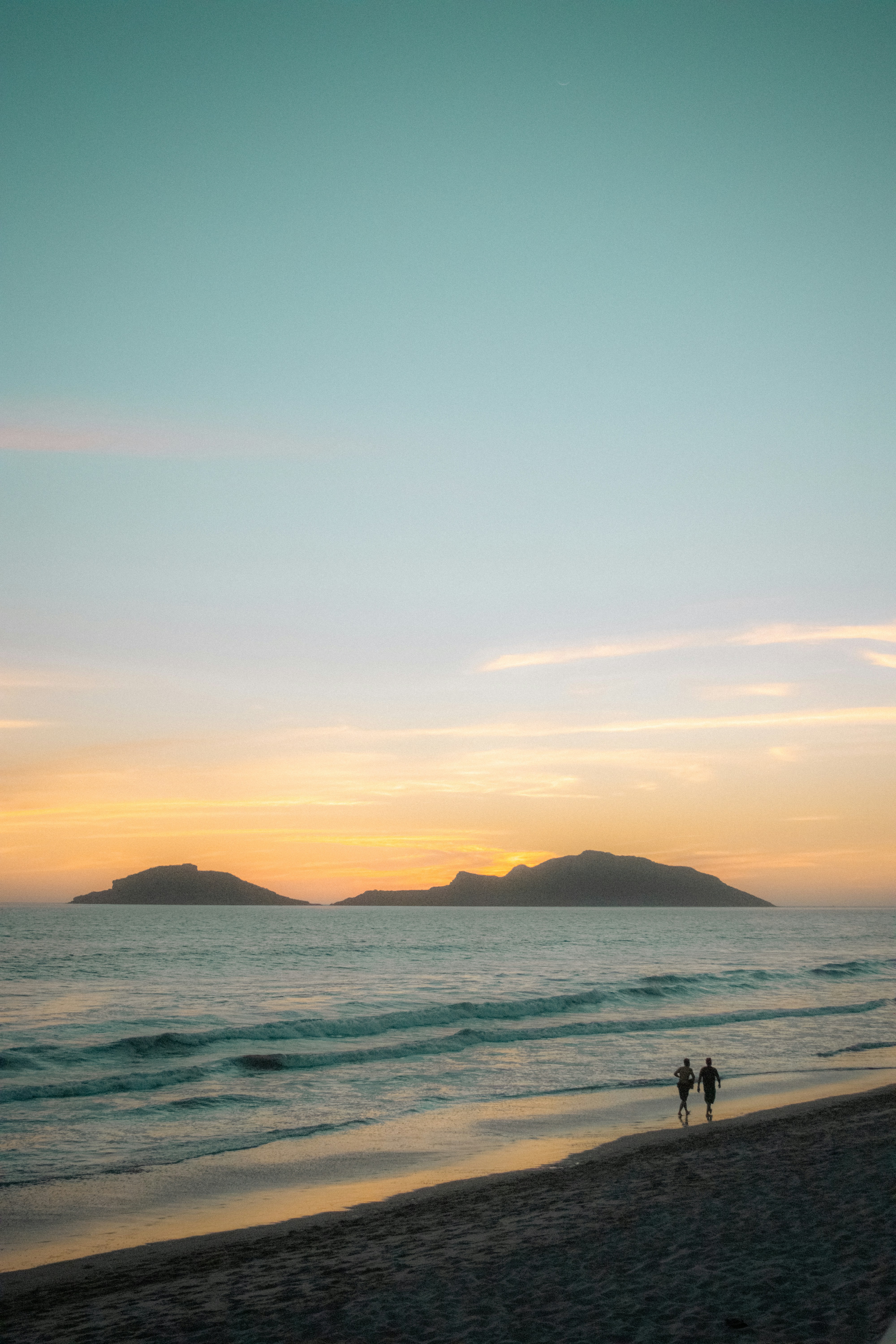 A couple of people standing on top of a sandy beach