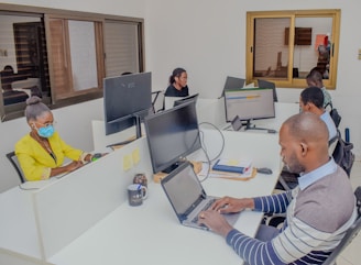 A group of people sitting around a table with laptops
