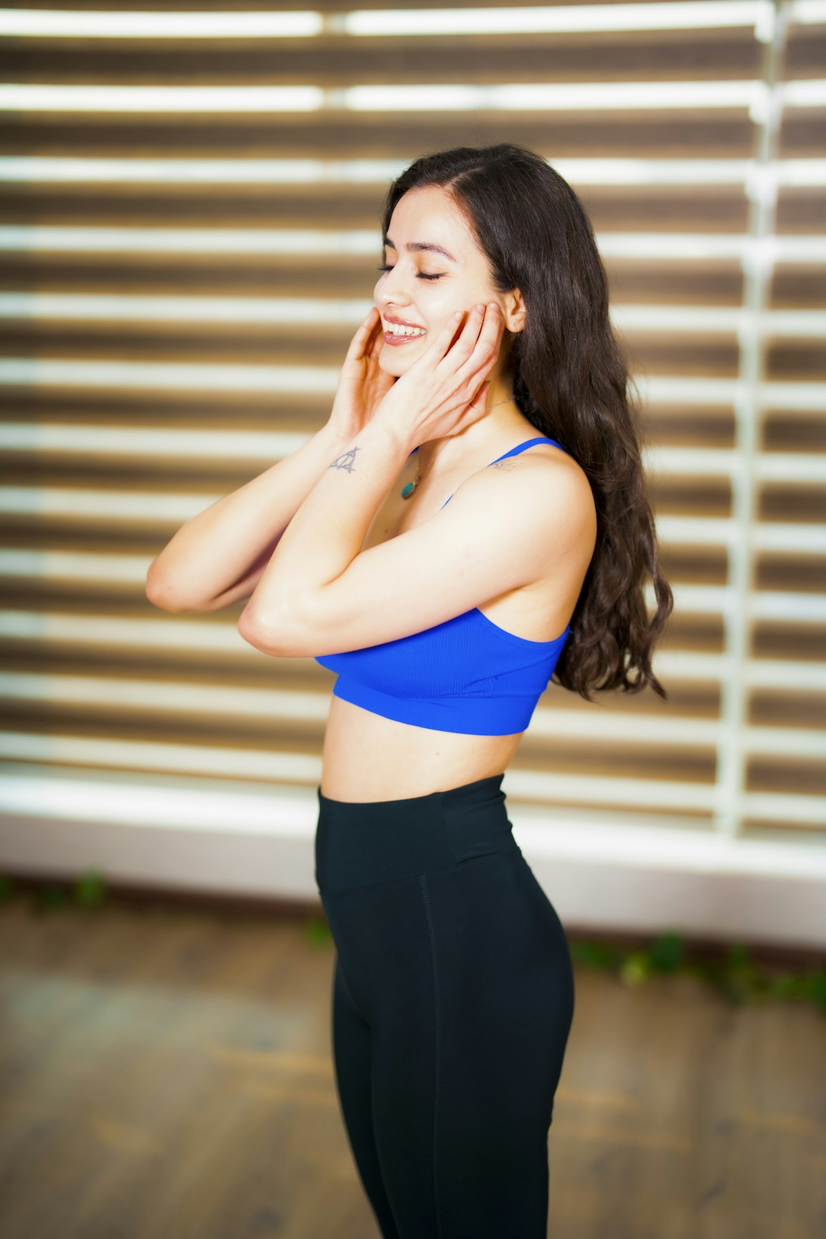 양 손바닥을 볼에 대고 미소 지으며 얼굴 리프팅 운동을 하는 여성