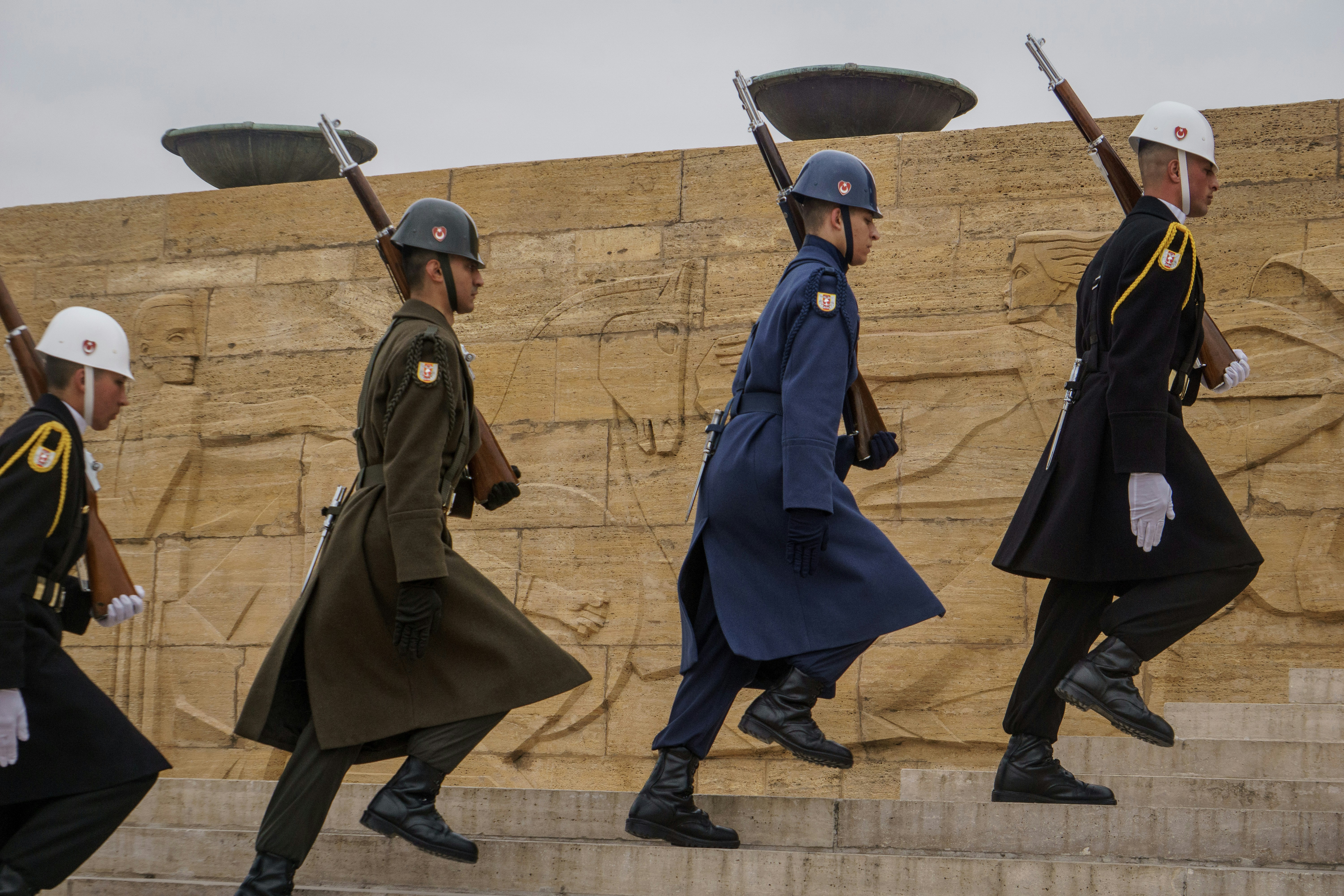 A group of men walking down a street next to a stone wall