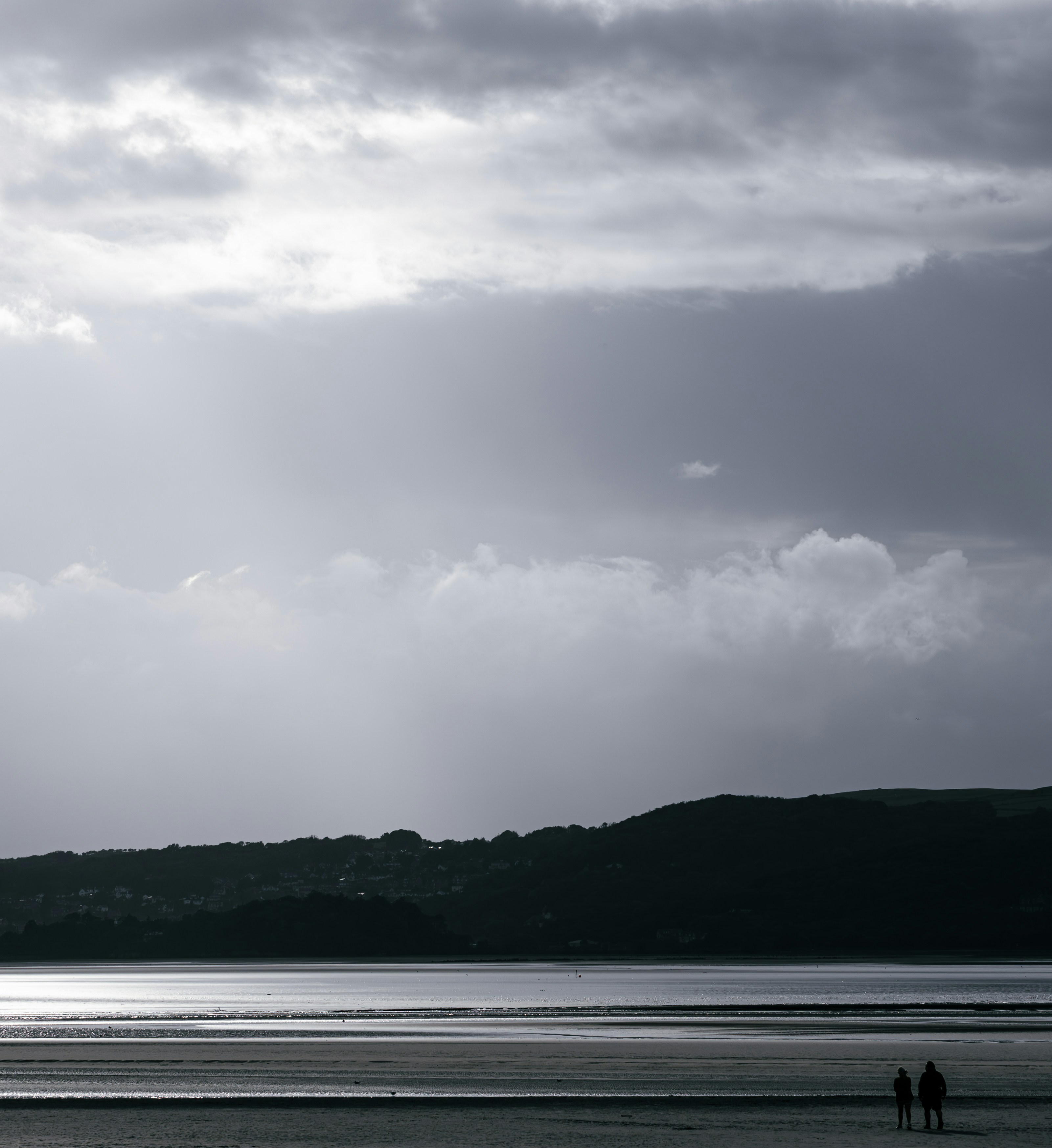 Two people walking on a beach under a cloudy sky