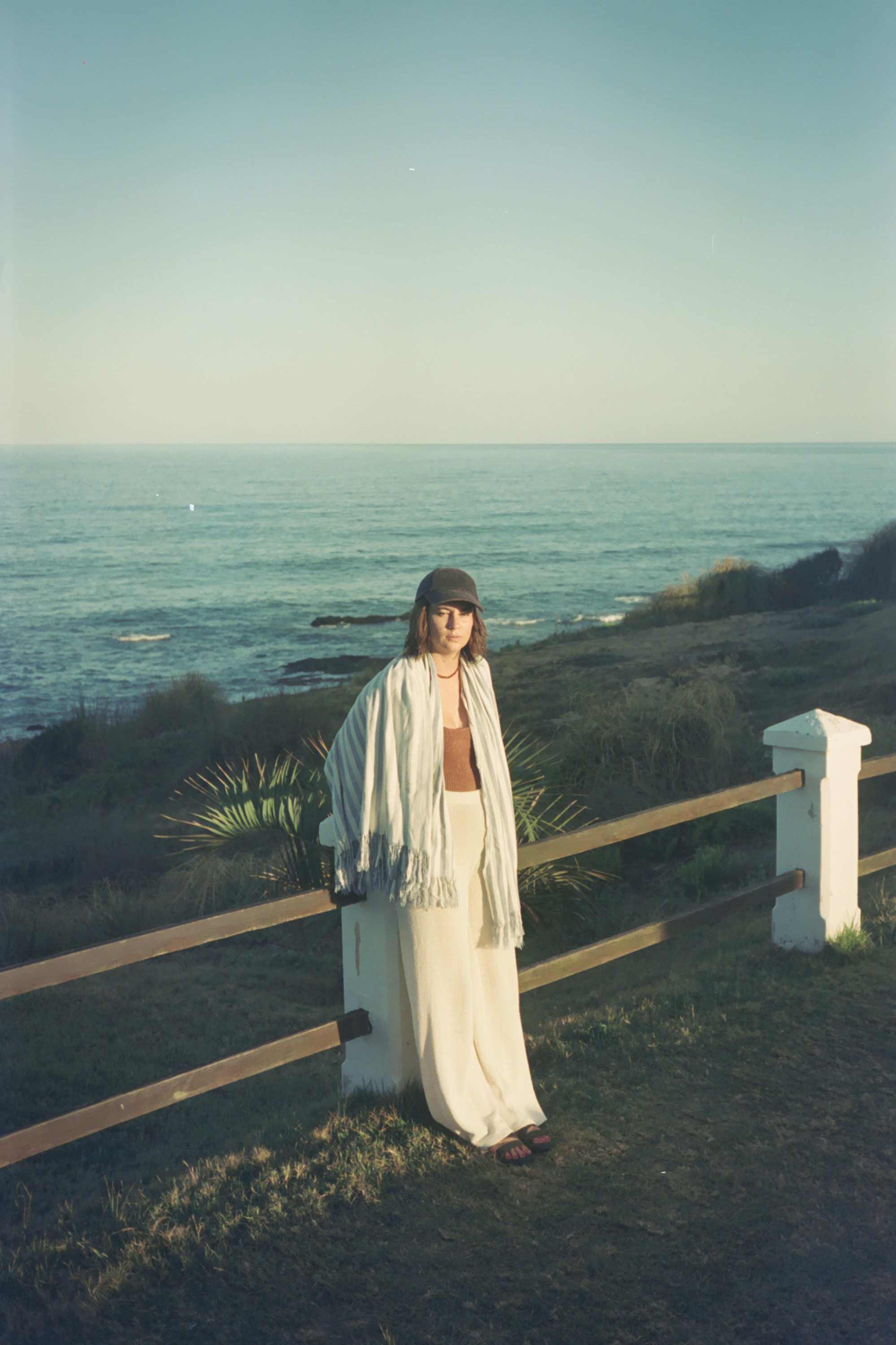 A woman in a white dress standing by a fence
