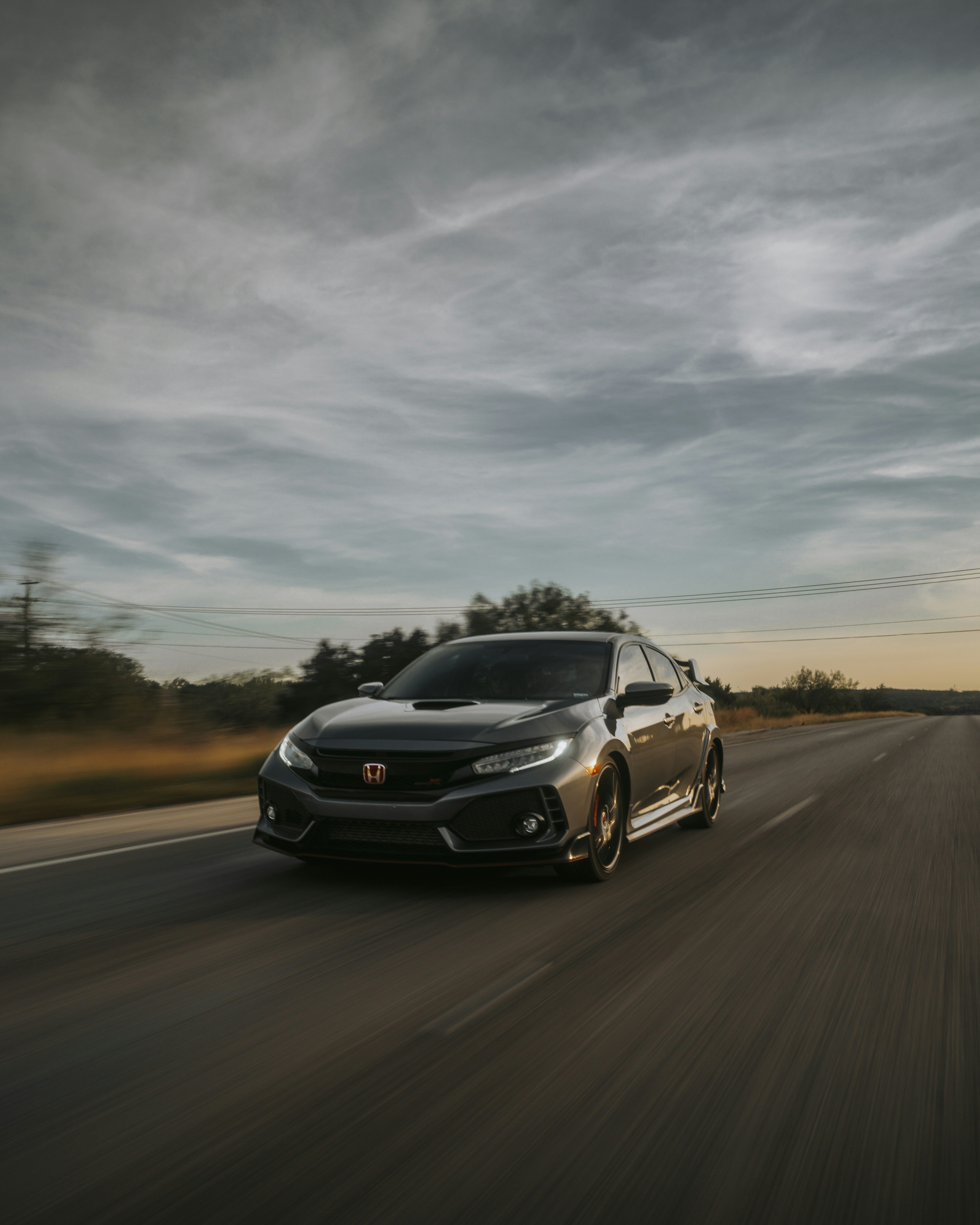 A black car driving down a road under a cloudy sky