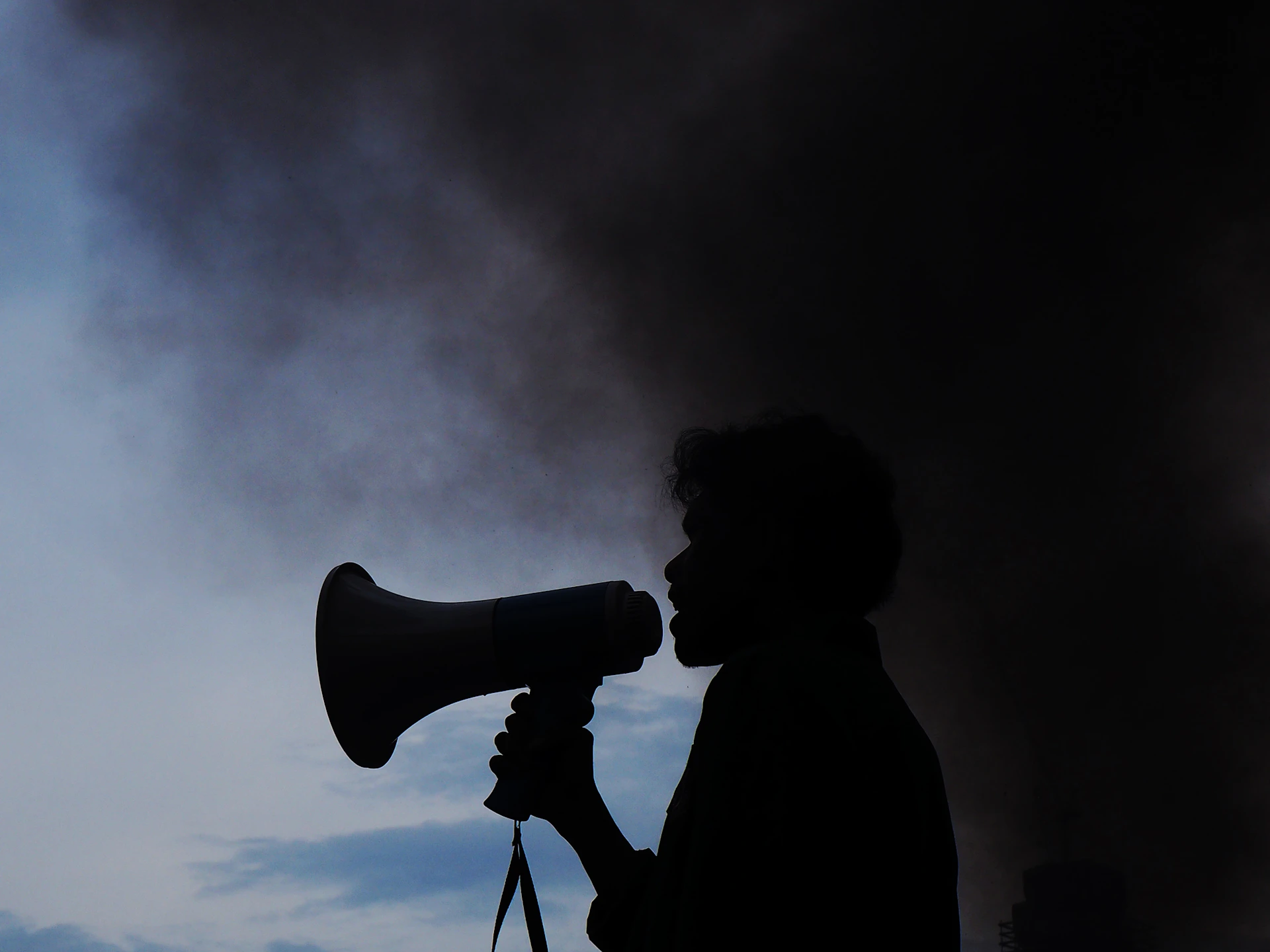 A silhouette of a man holding a megaphone in front of a cloud of smoke