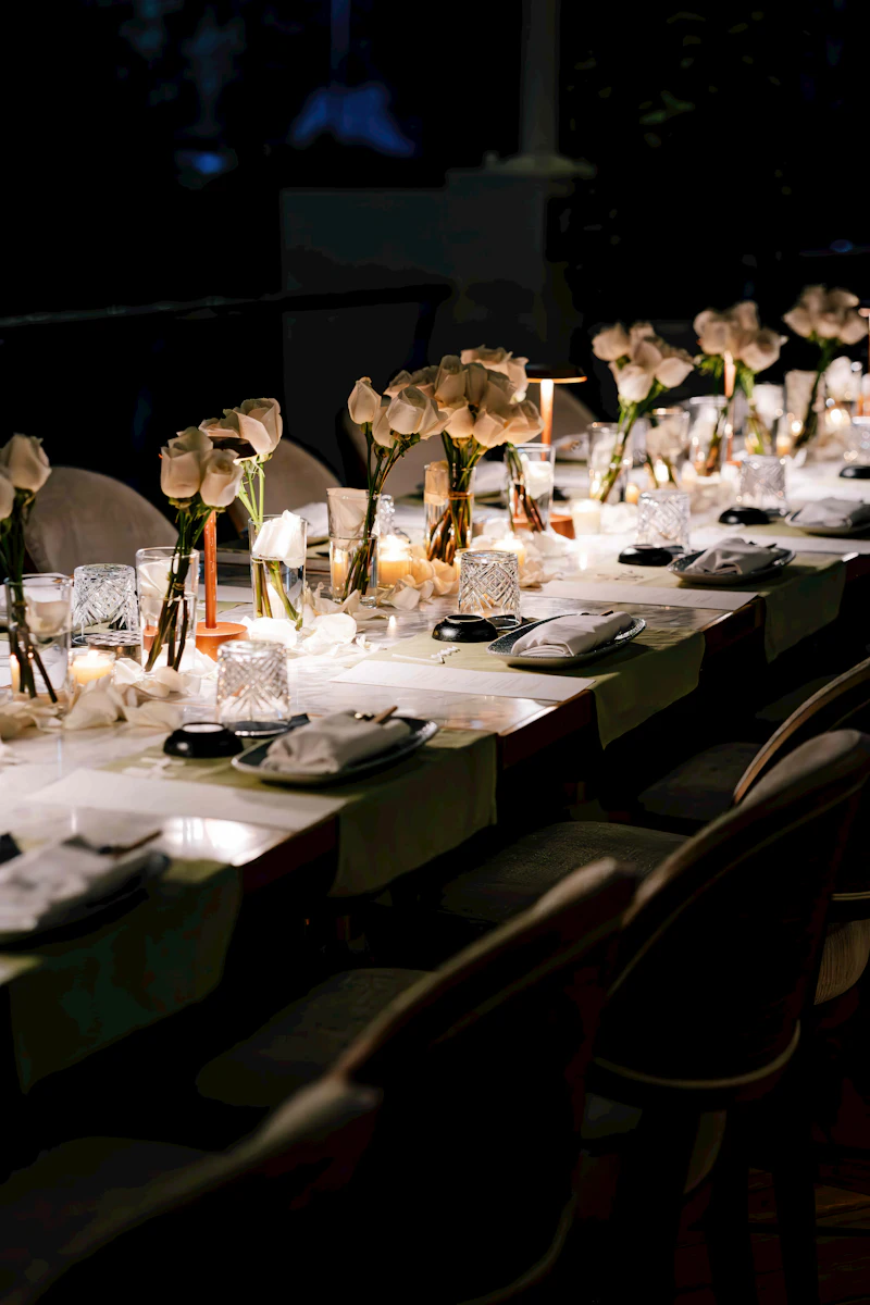 A long banquet table set with flowers and lit candles glowing in the evening at a wedding reception