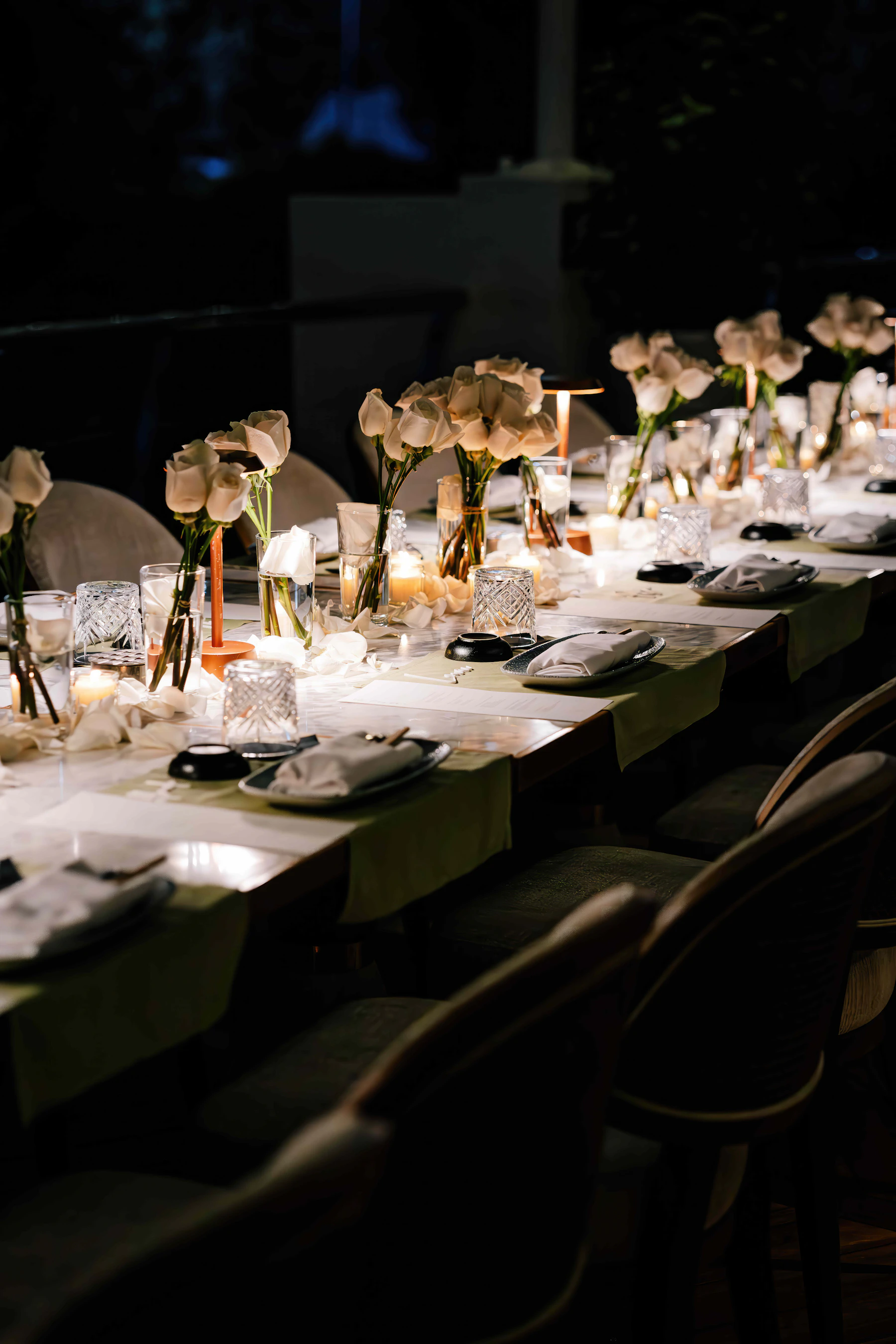 A long dinner table set with white roses and candlelight