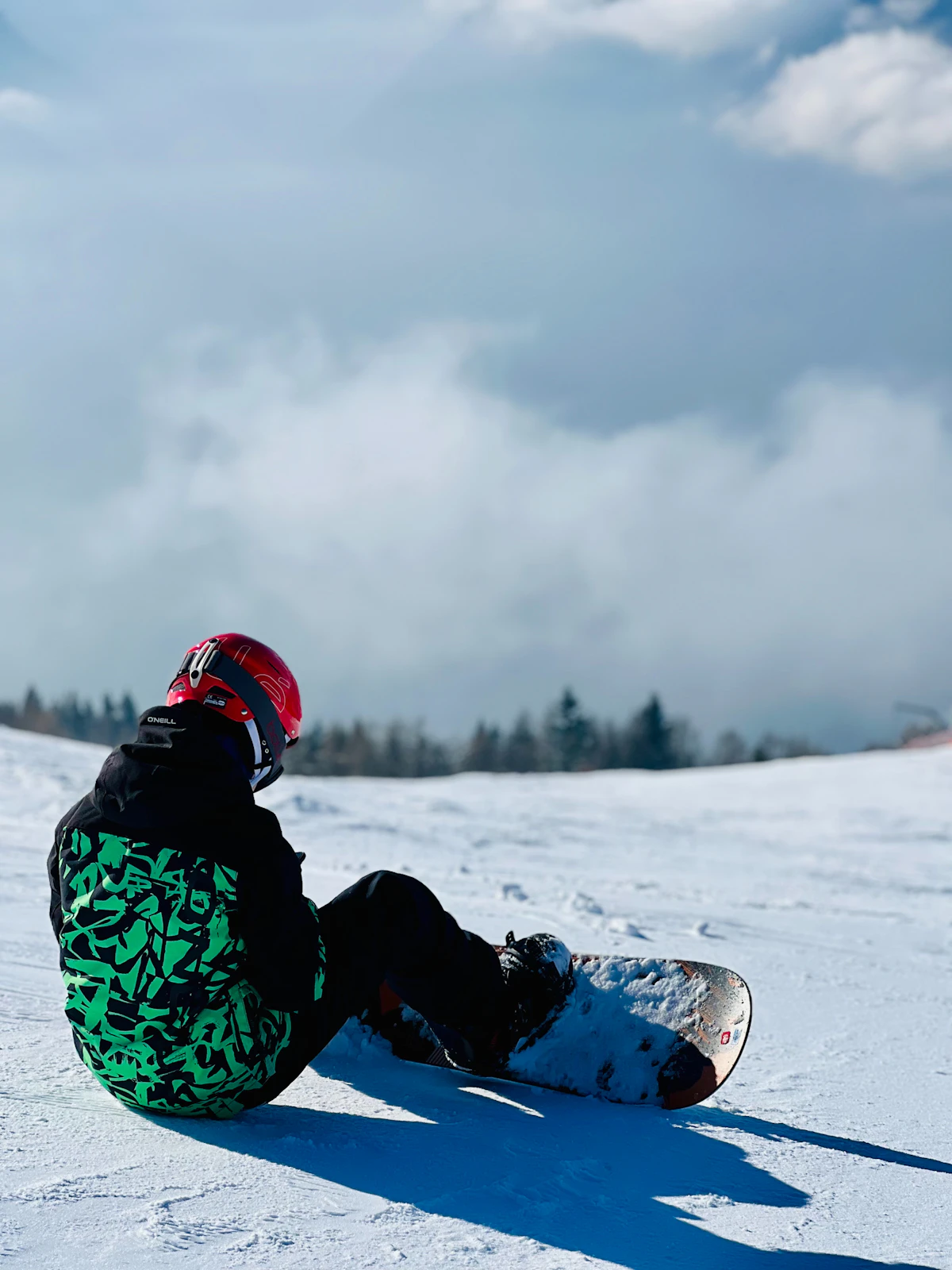 Người học snowboard ngồi trên tuyết, chân vẫn gắn ván