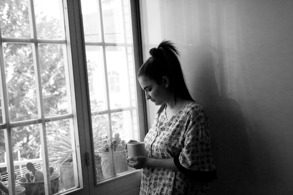 A woman standing in front of a window holding a cup