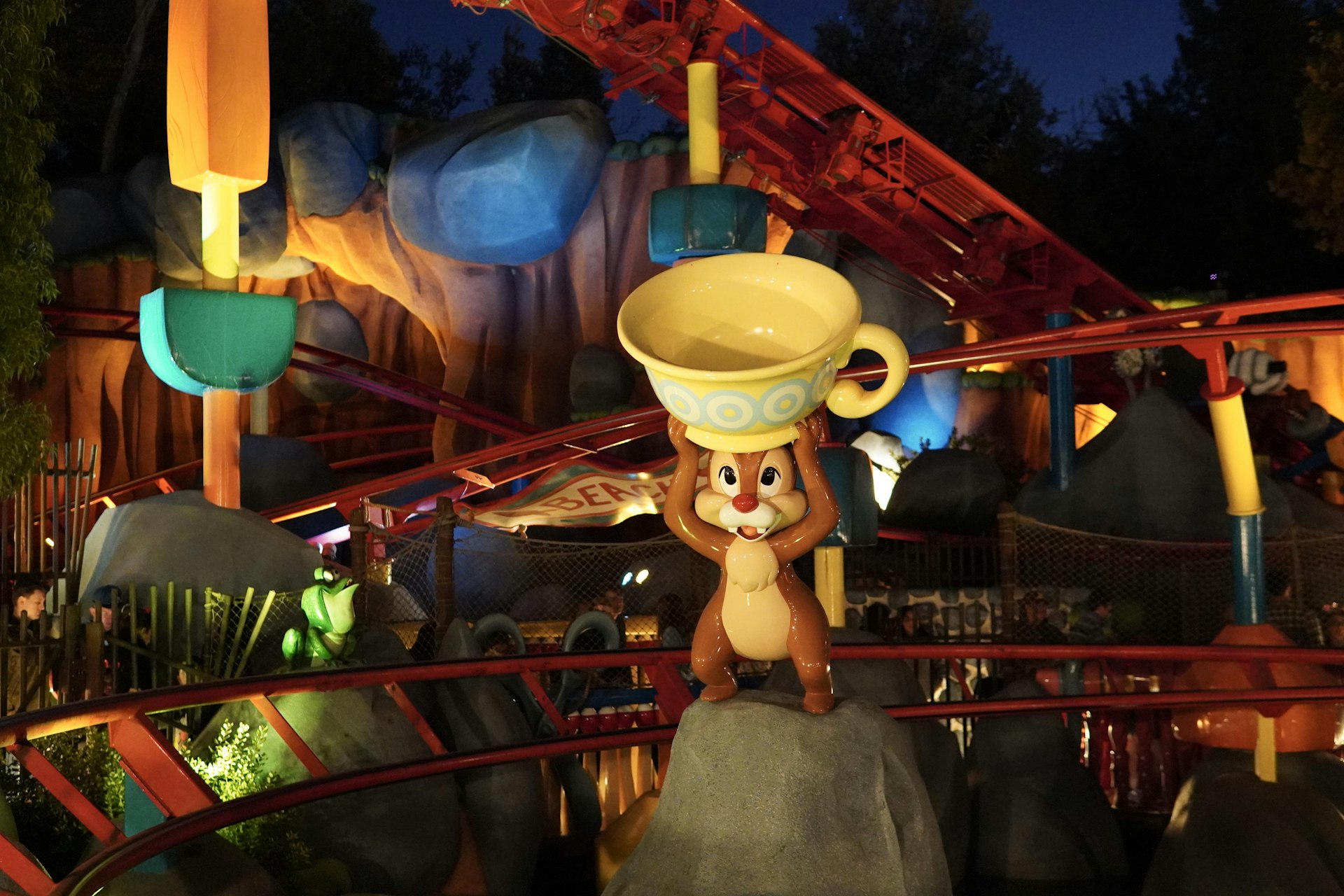 A small squirrel on top of a rock in front of a roller coaster