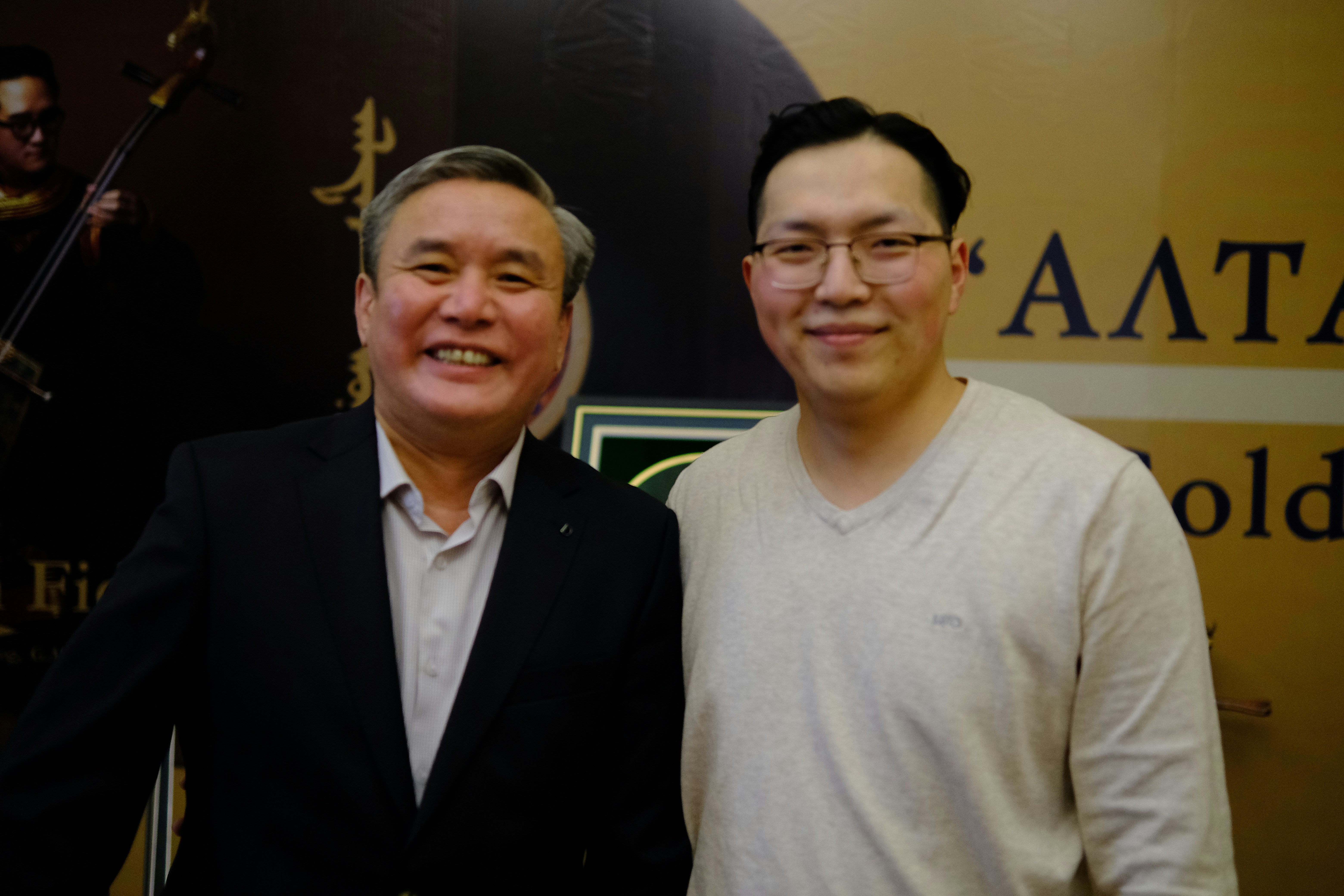 Two men standing next to each other in front of a sign