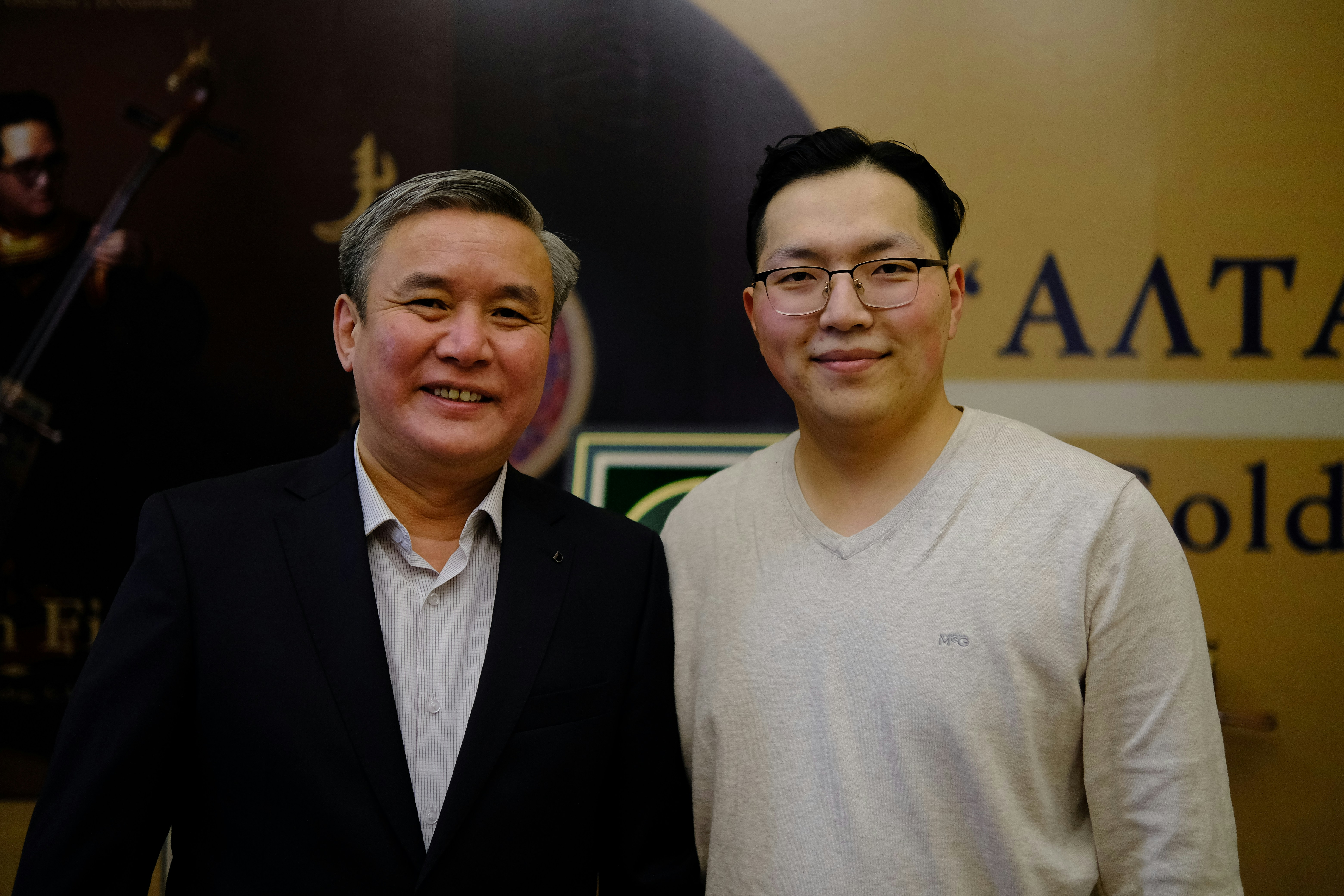 Two men standing next to each other in front of a sign