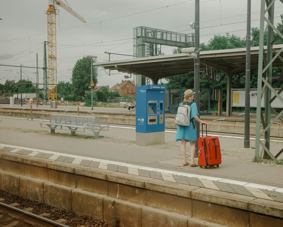 Voyageuse avec un sac à dos et une valise orange qui attend seule sur le quai d'une gare