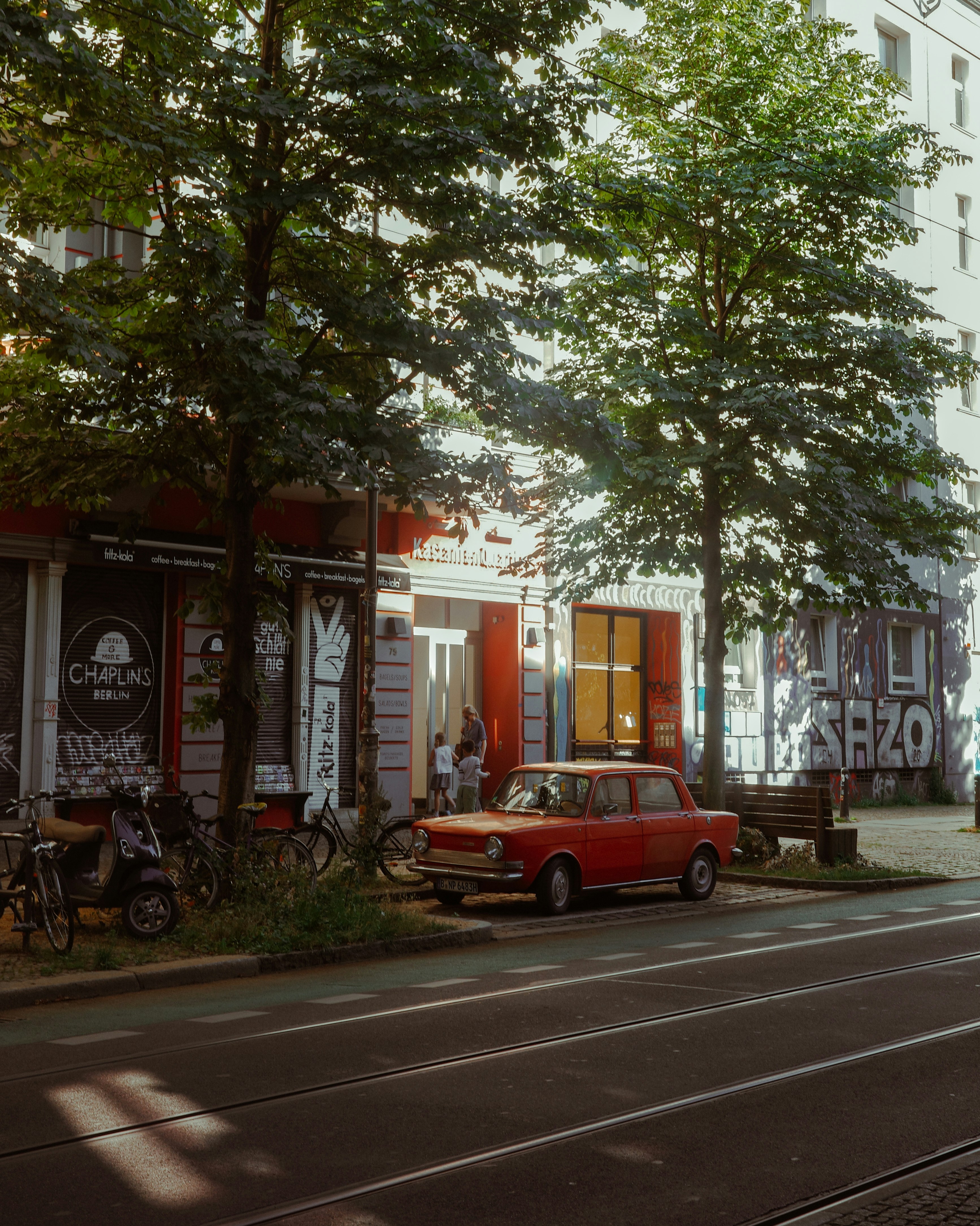 A red car driving down a street next to tall buildings
