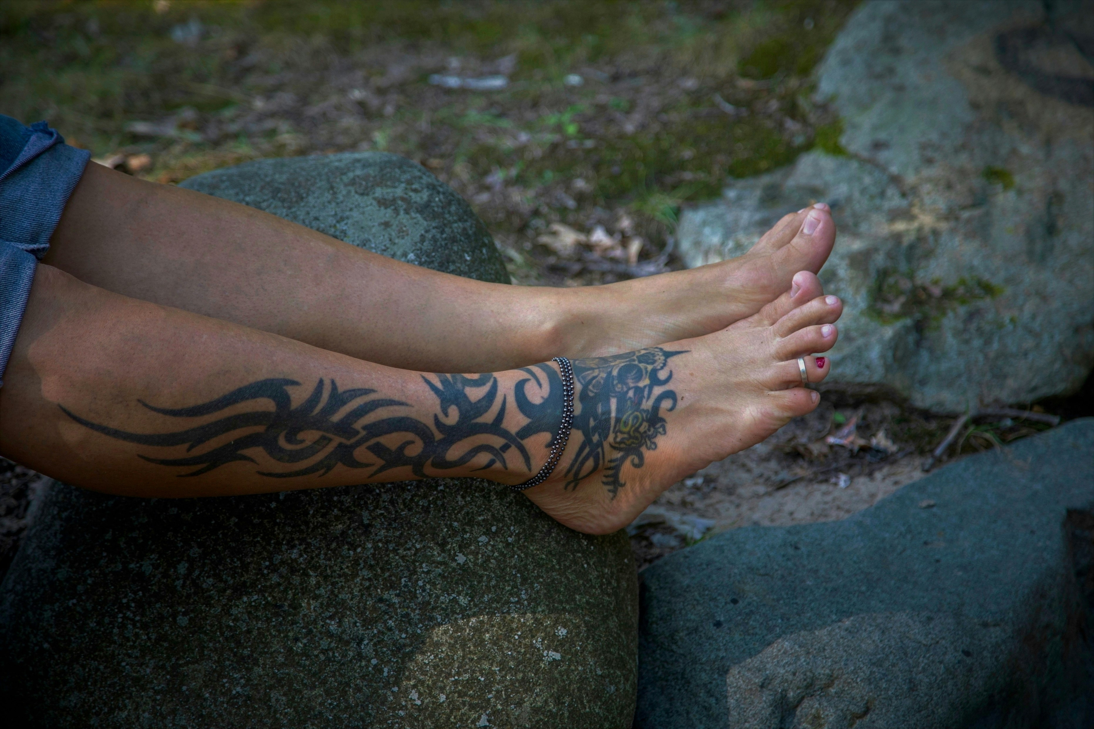 A person with a tattoo on their foot sitting on a rock