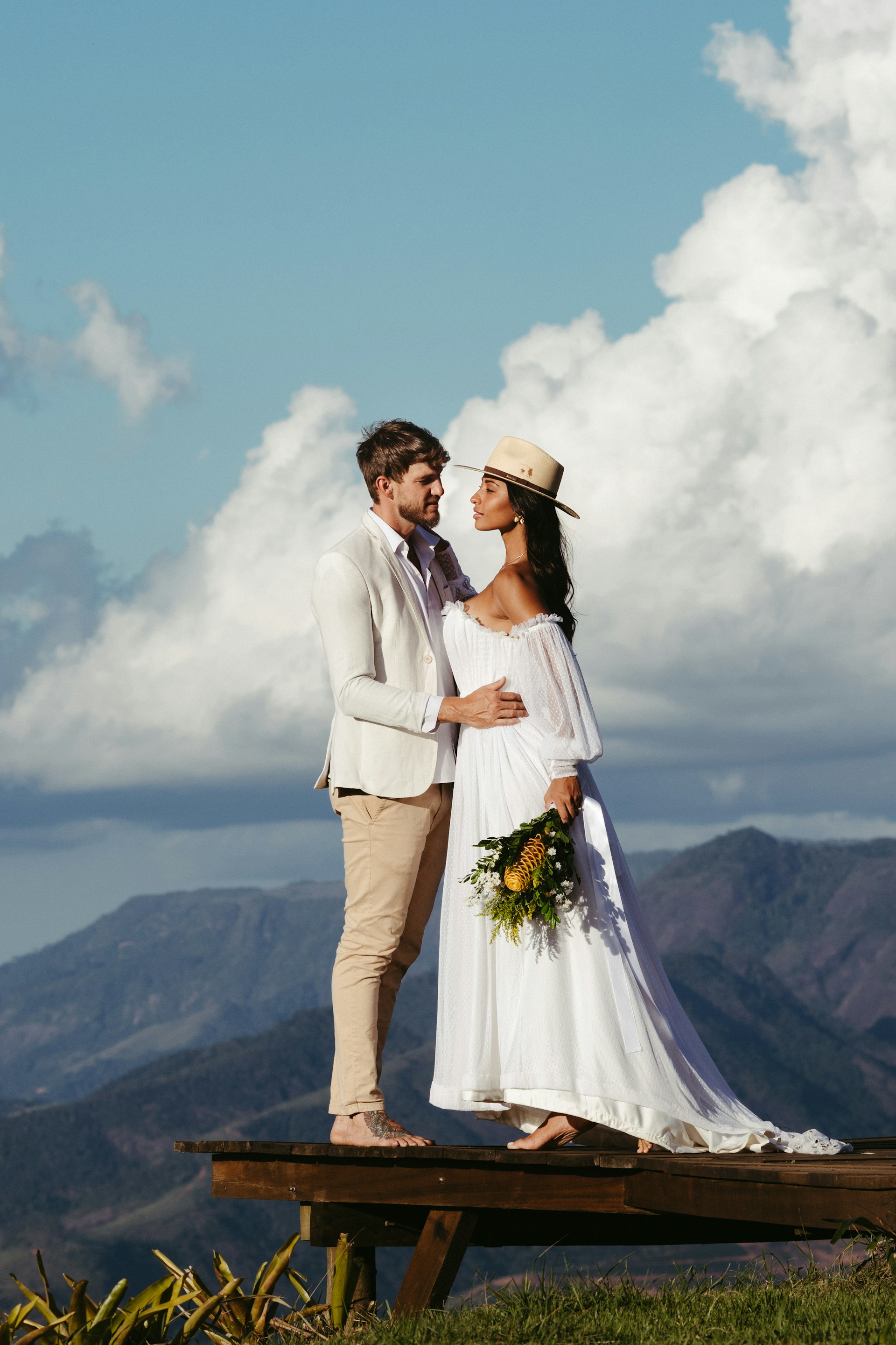 A bride and groom standing on a bench at the top of a mountain