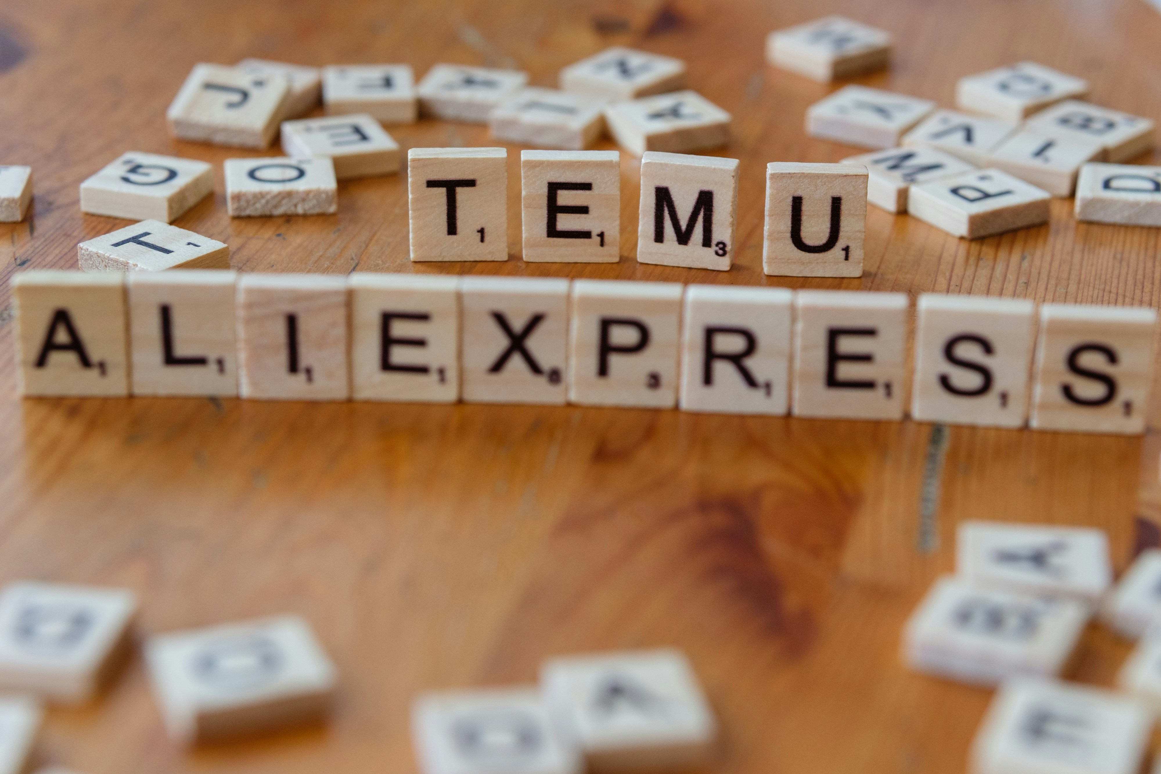 Scrabble tiles spelling the word temu allexpress on a wooden table
