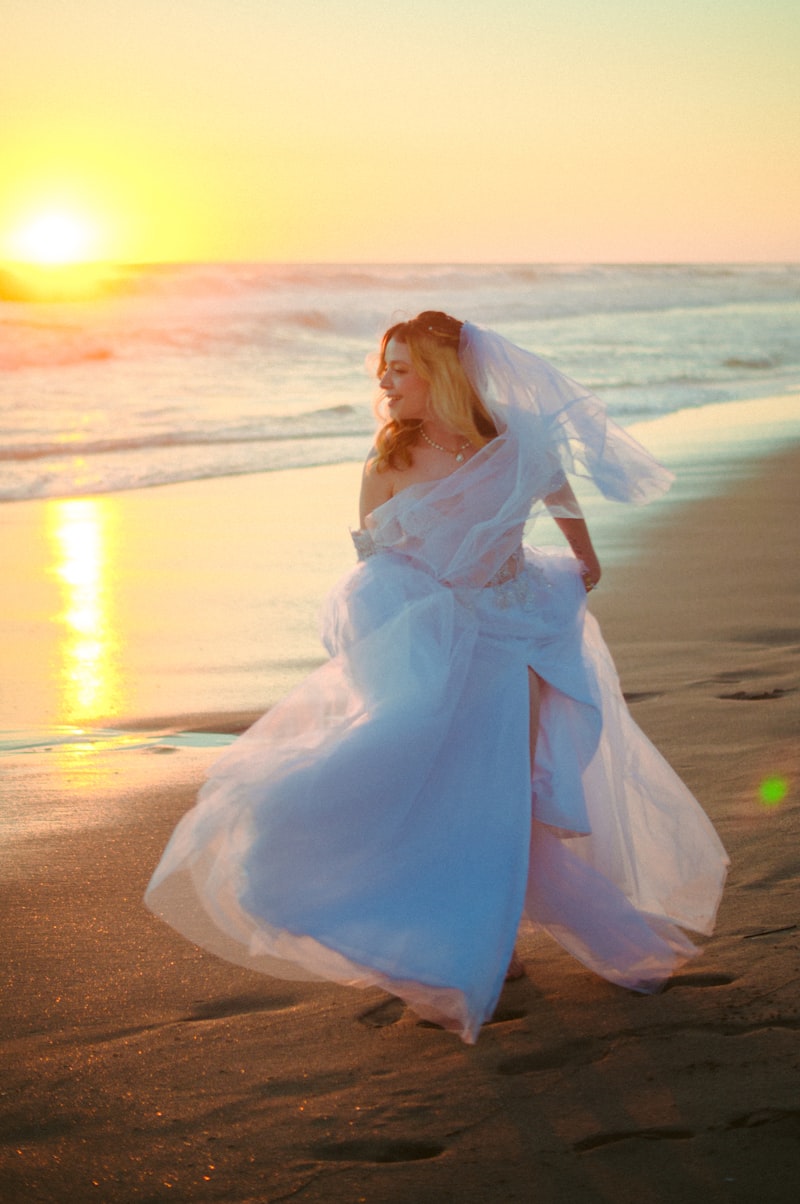 Bride in flowing white dress on beach at golden hour sunset