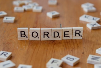 Scrabbled letters spelling the word border on a wooden table