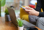 A person using a cell phone while sitting in front of a laptop