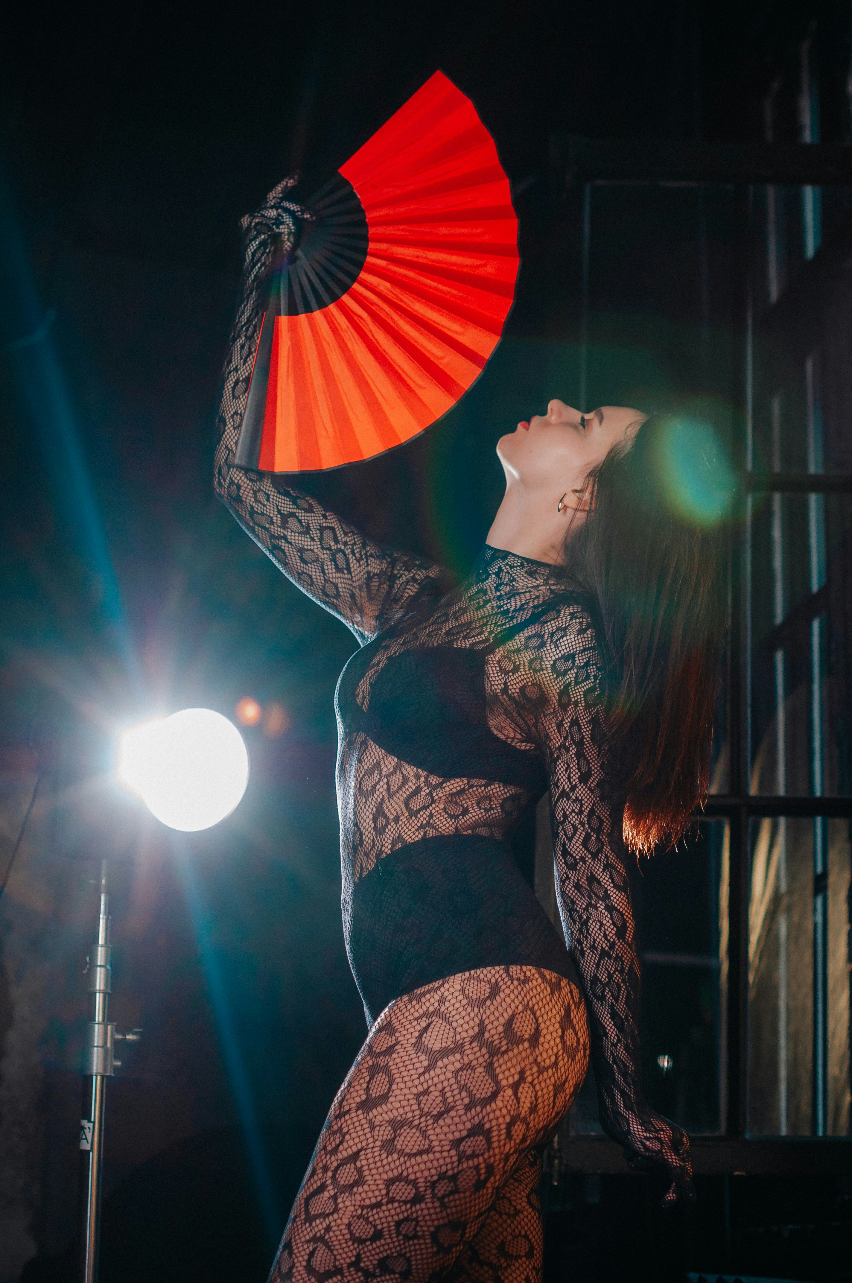 A woman in a bodysuit holding a red fan