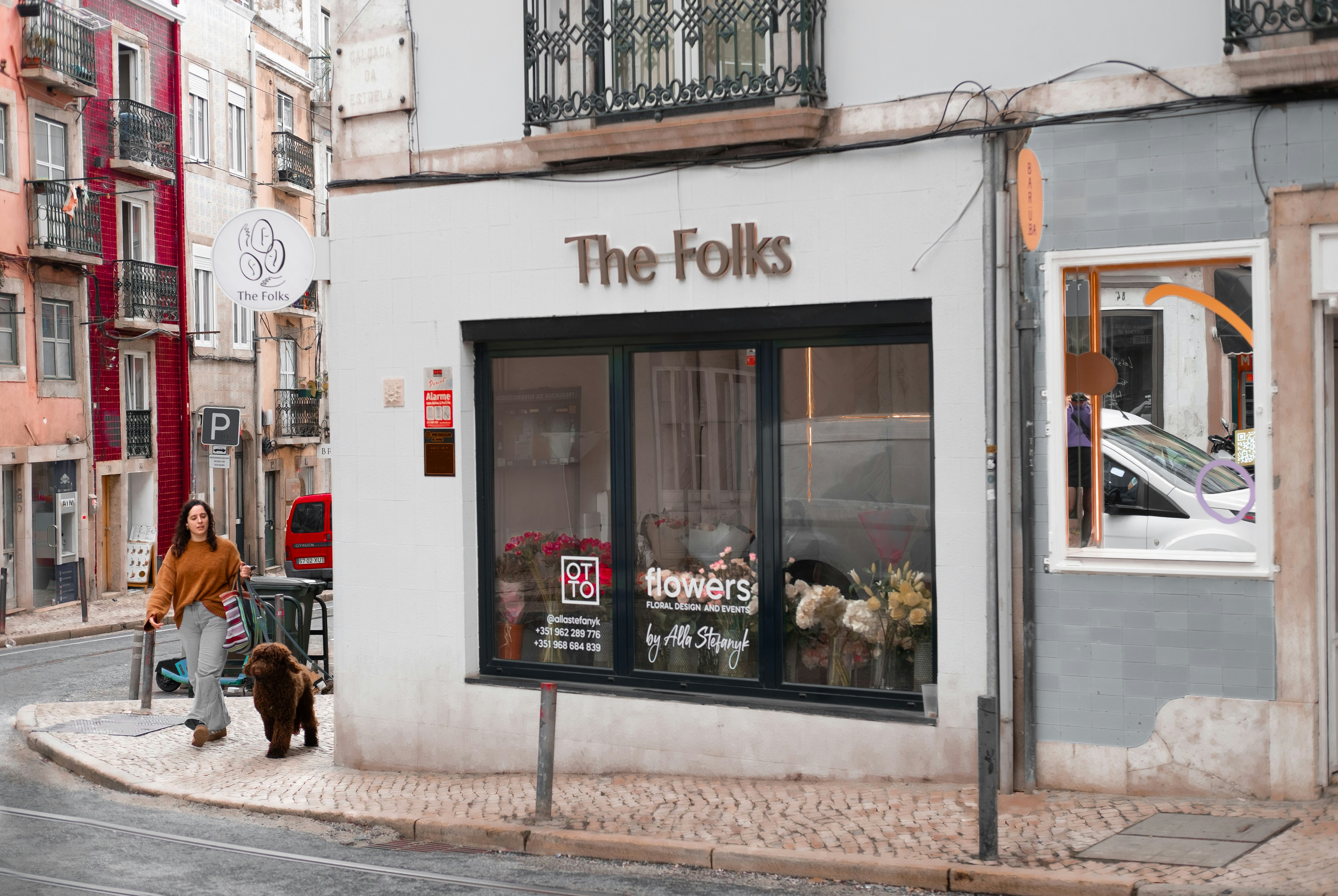 A man walking a dog down a street past a store