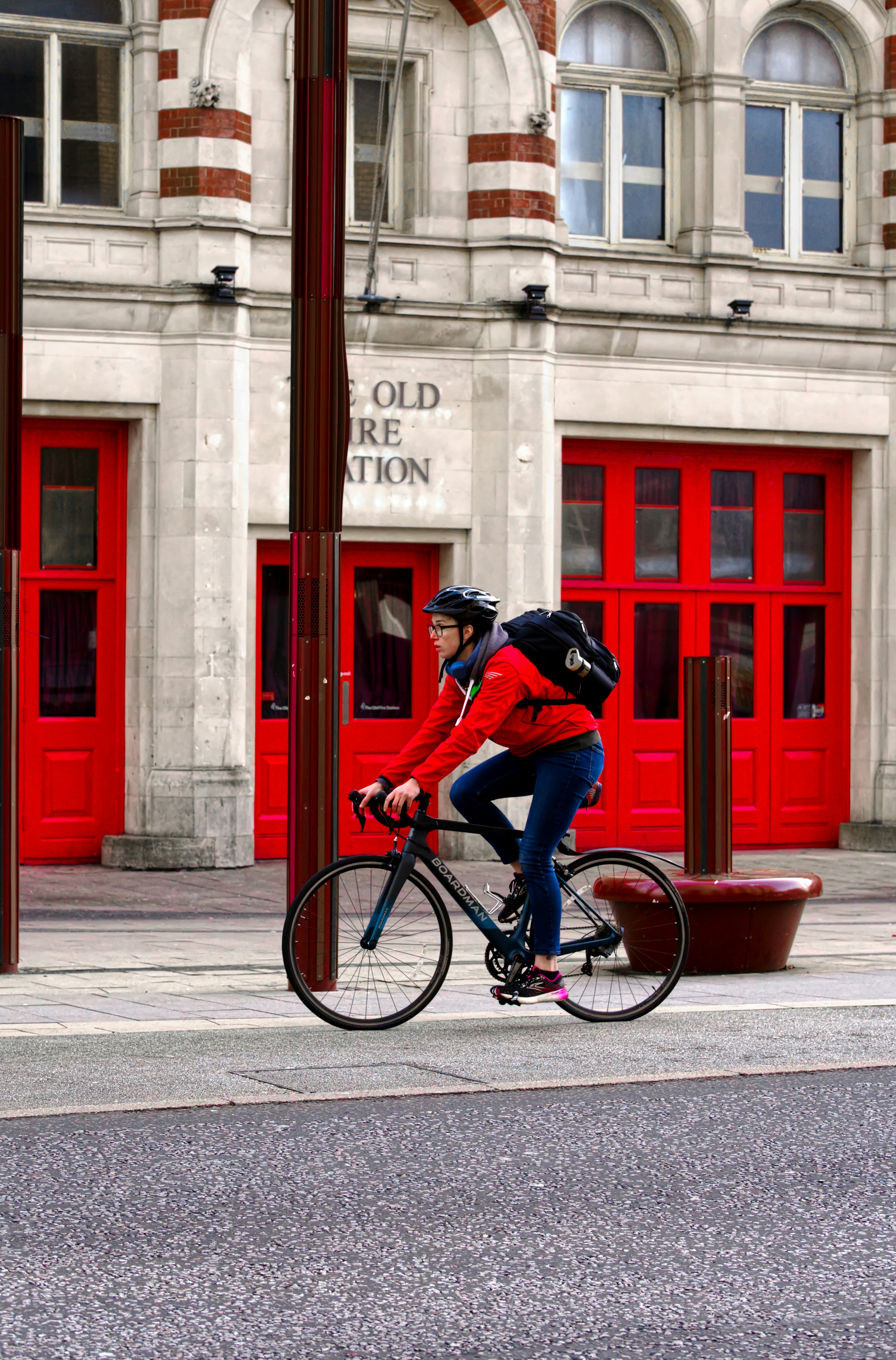 赤い建物の前を自転車で通り過ぎる男性