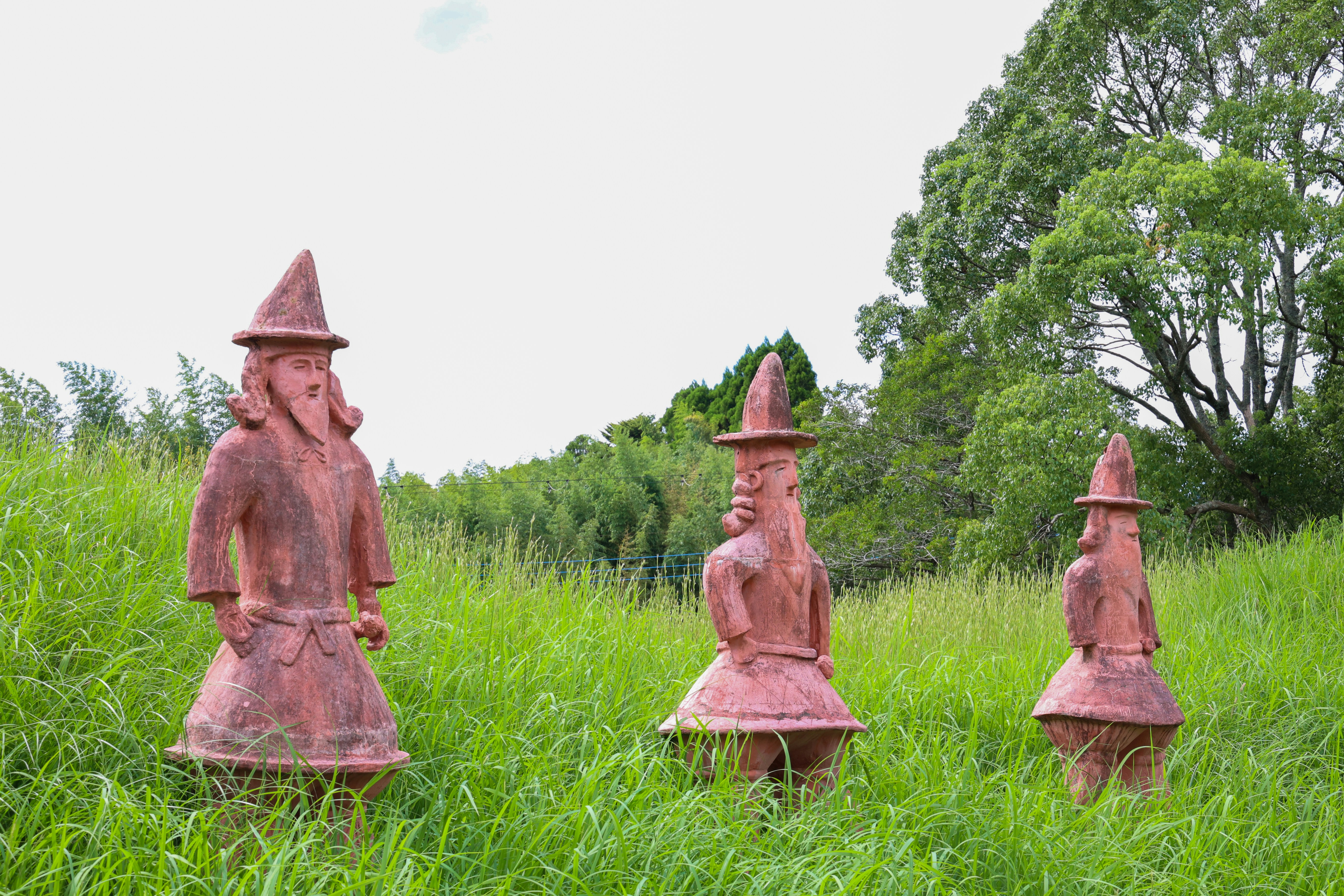 A group of red statues sitting on top of a lush green field