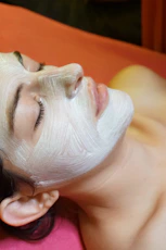 A woman with a facial mask on laying on a bed