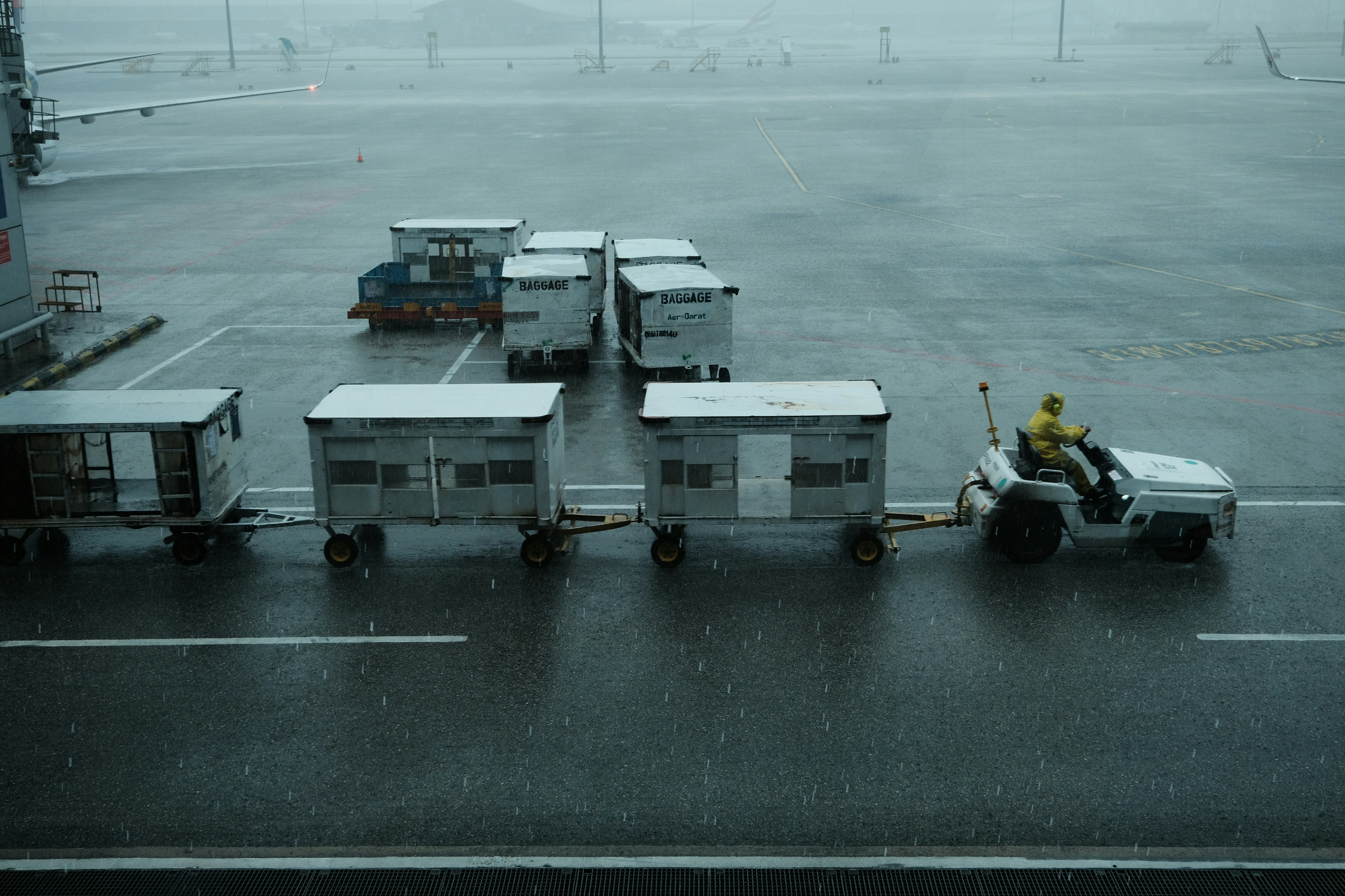 A man is sitting on a luggage cart in the rain, 