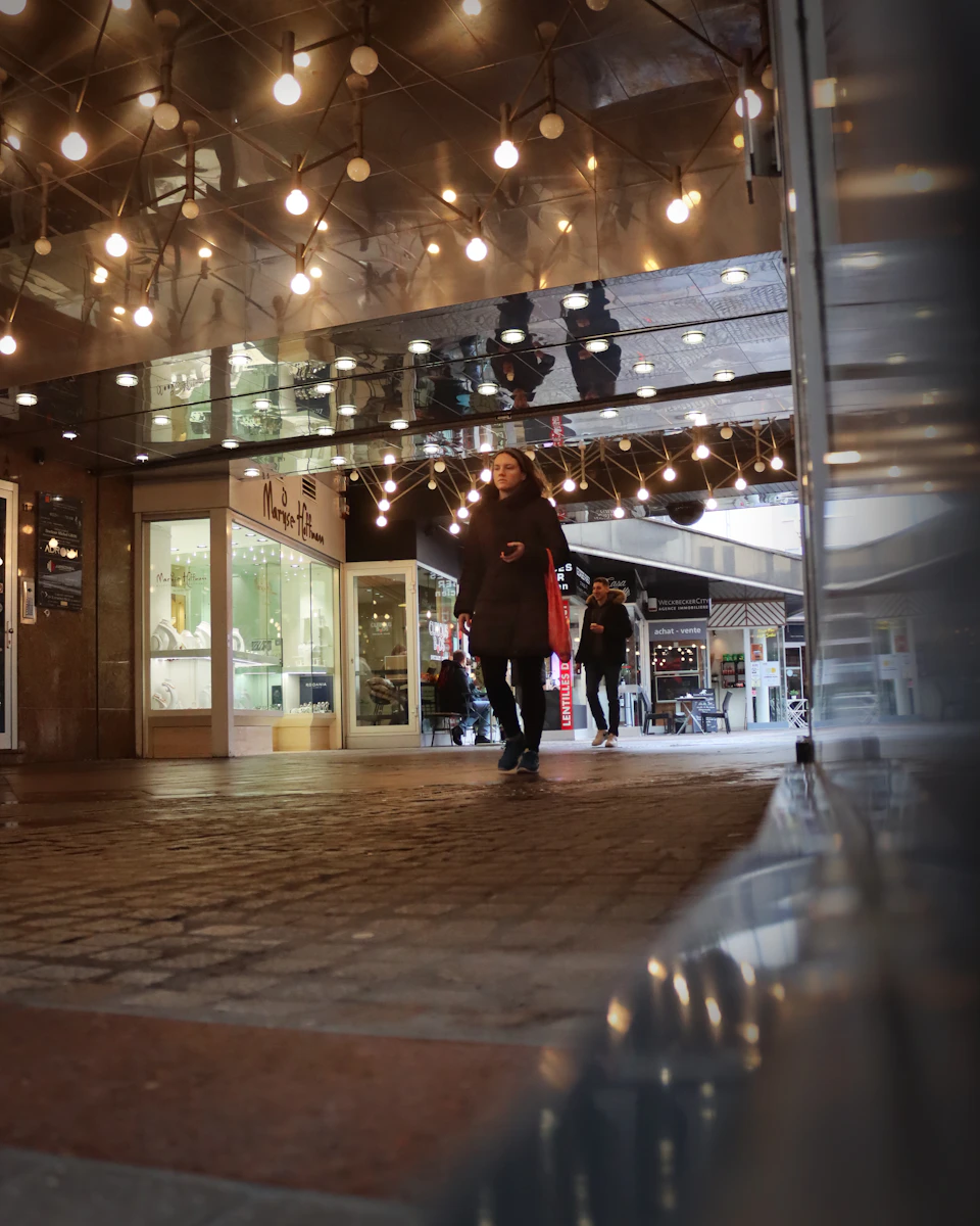 Bustling shopping center with people browsing stores through large windows reflecting street activity