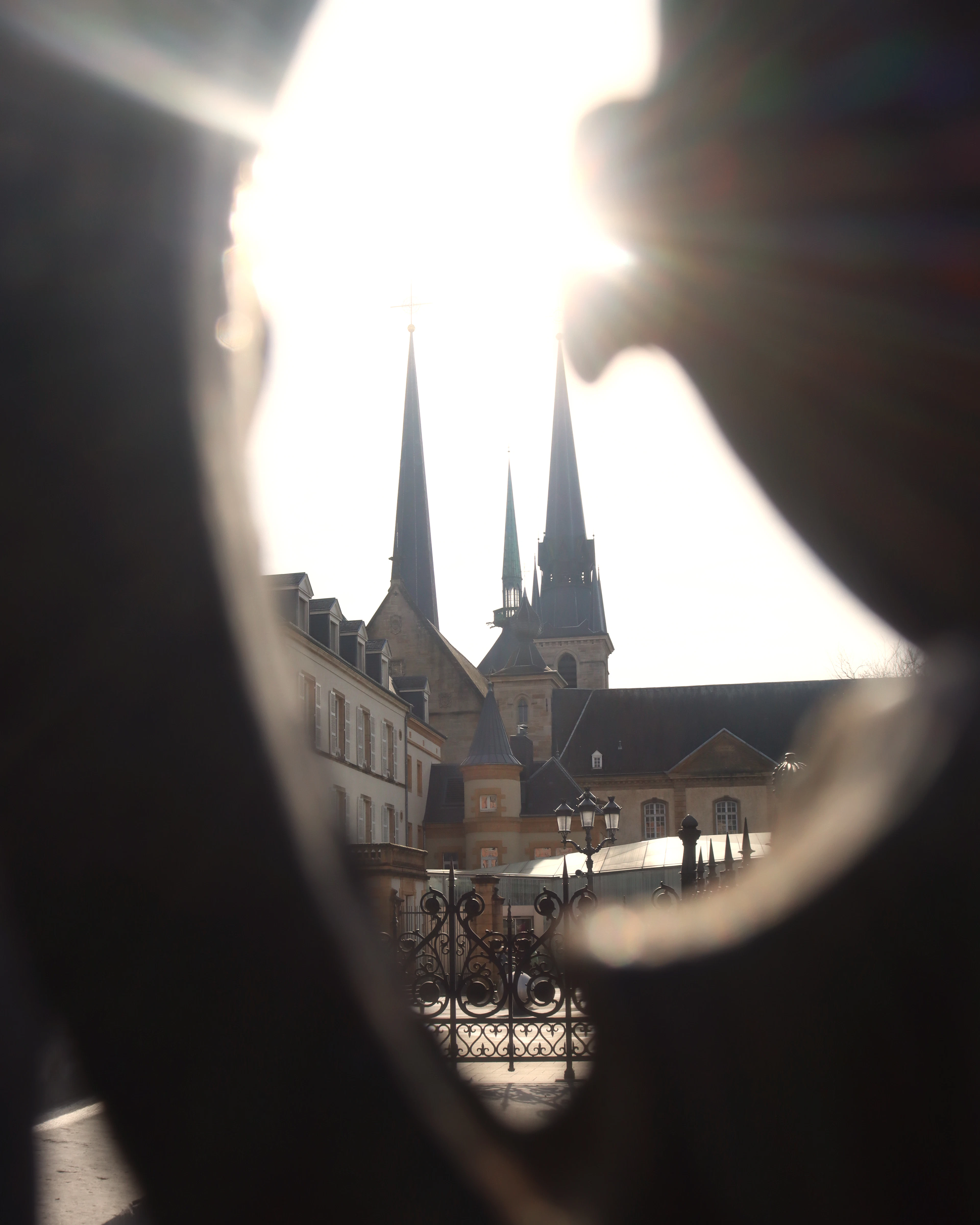 Backlit church spires glow behind a dark curved silhouette in the foreground, with the sun flaring overhead.