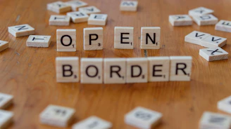 A wooden table topped with scrabble tiles spelling open border