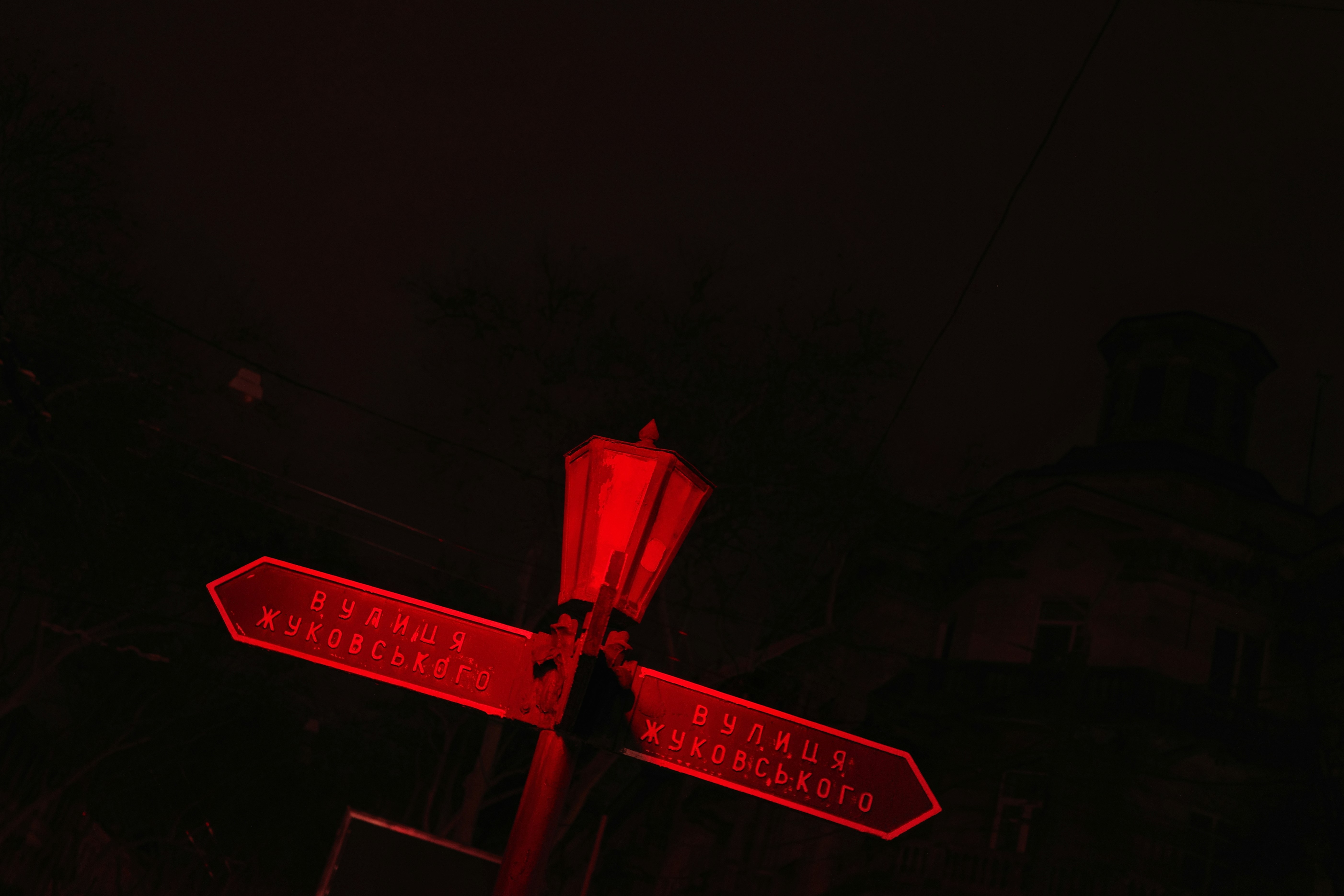 A crossroads bathed in an eerie red glow. The night is silent, but the sign speaks—two paths, one decision. Which way would you go?