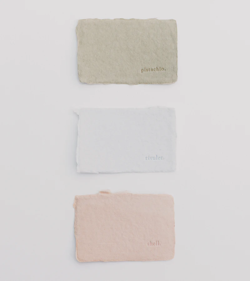 Three deckle-edged paper samples in sage, pale blue and blush, laid on white, each debossed with a colour name.