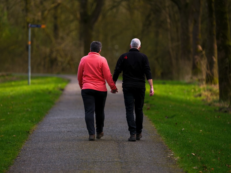 Older couple walking together holding hands on a forest path, demonstrating companionship and connection after 65