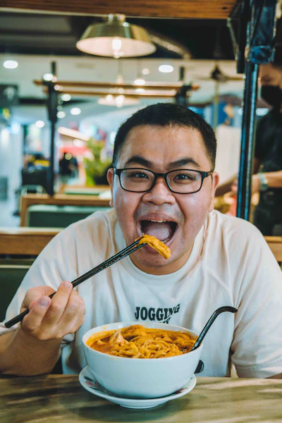A man sitting at a table with a bowl of noodles in front of him