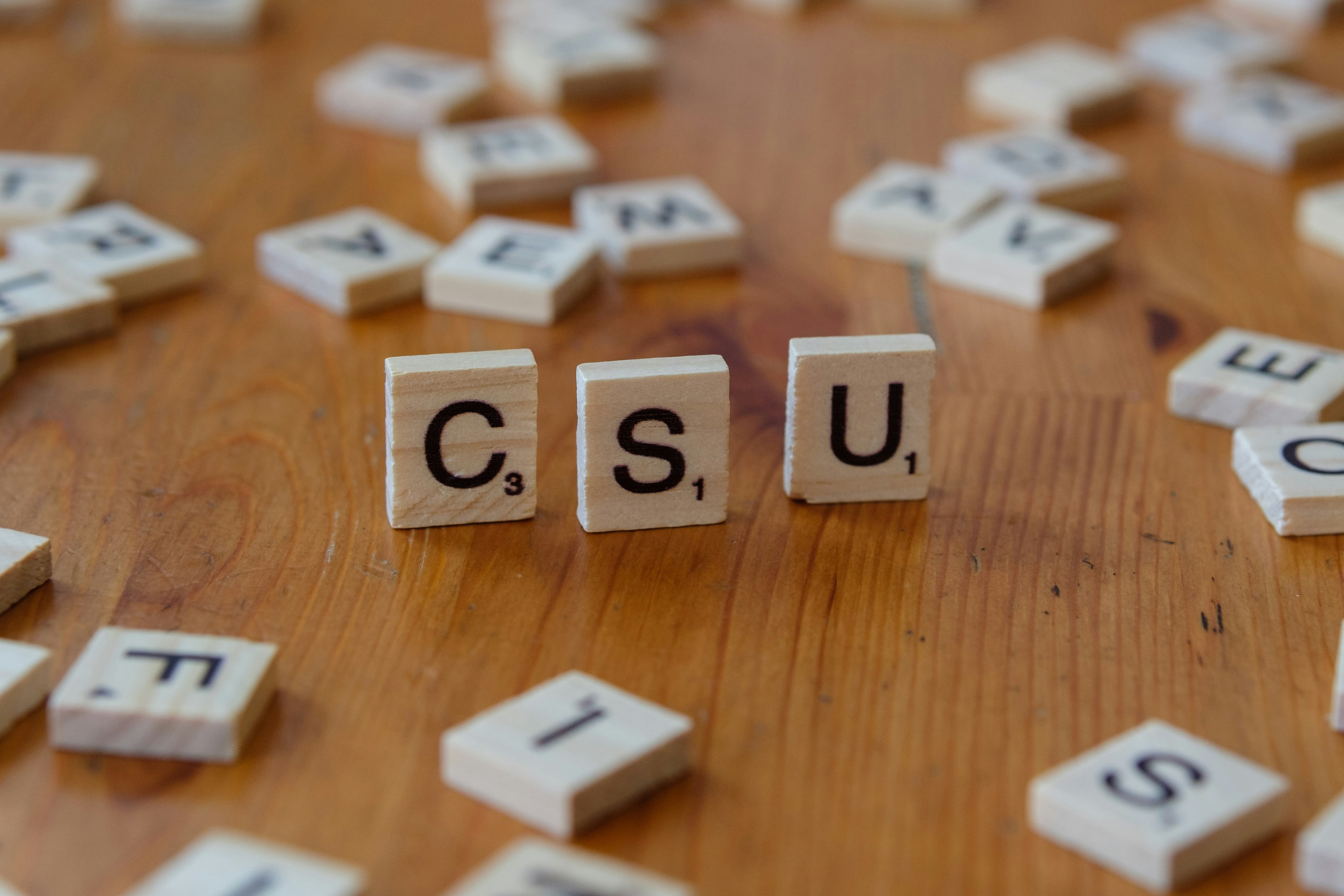 A wooden table topped with scrabble tiles spelling the word csu