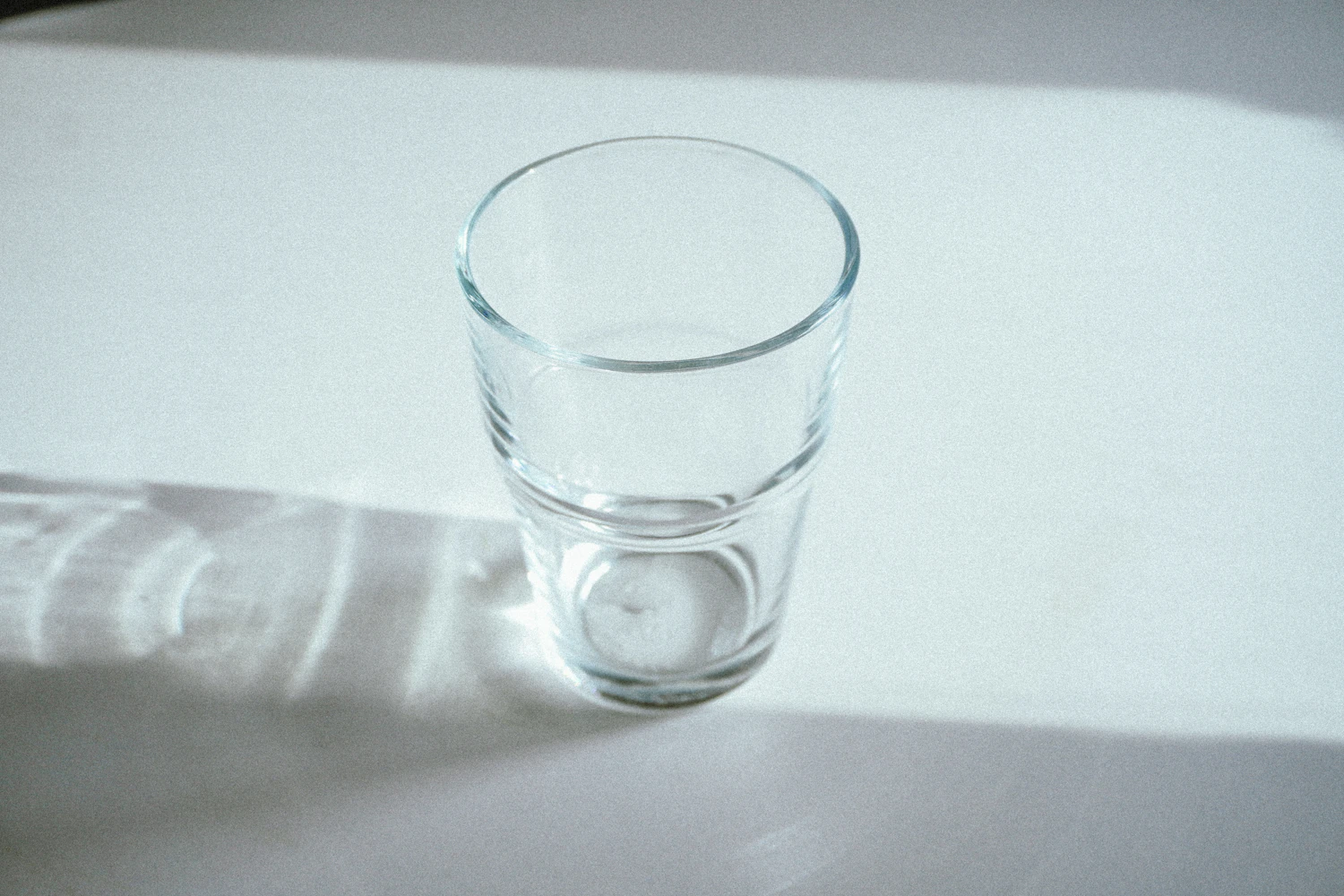 A small clear tumbler in a band of sunlight on a pale table