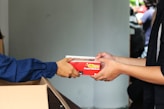 A person handing a box of pizza to another person
