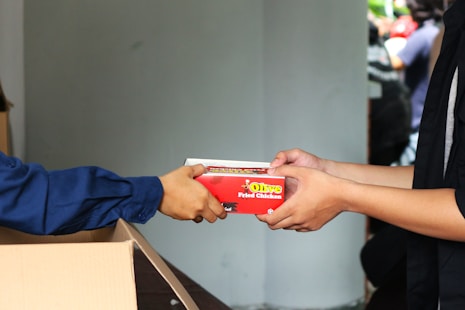 A person handing a box of pizza to another person