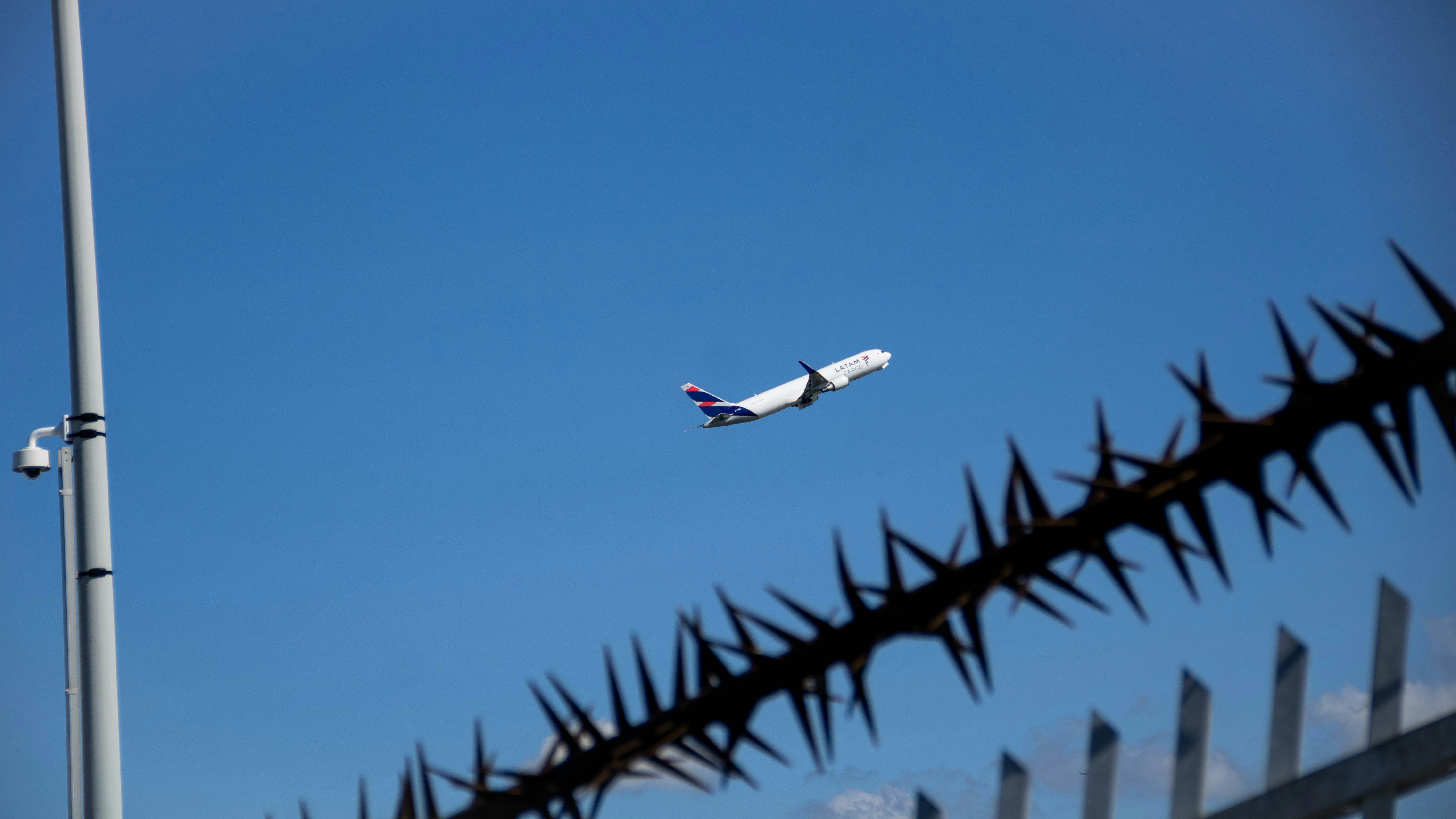 A plane flying over a fence with a sky background, Aircraft taking off behind a security fence.