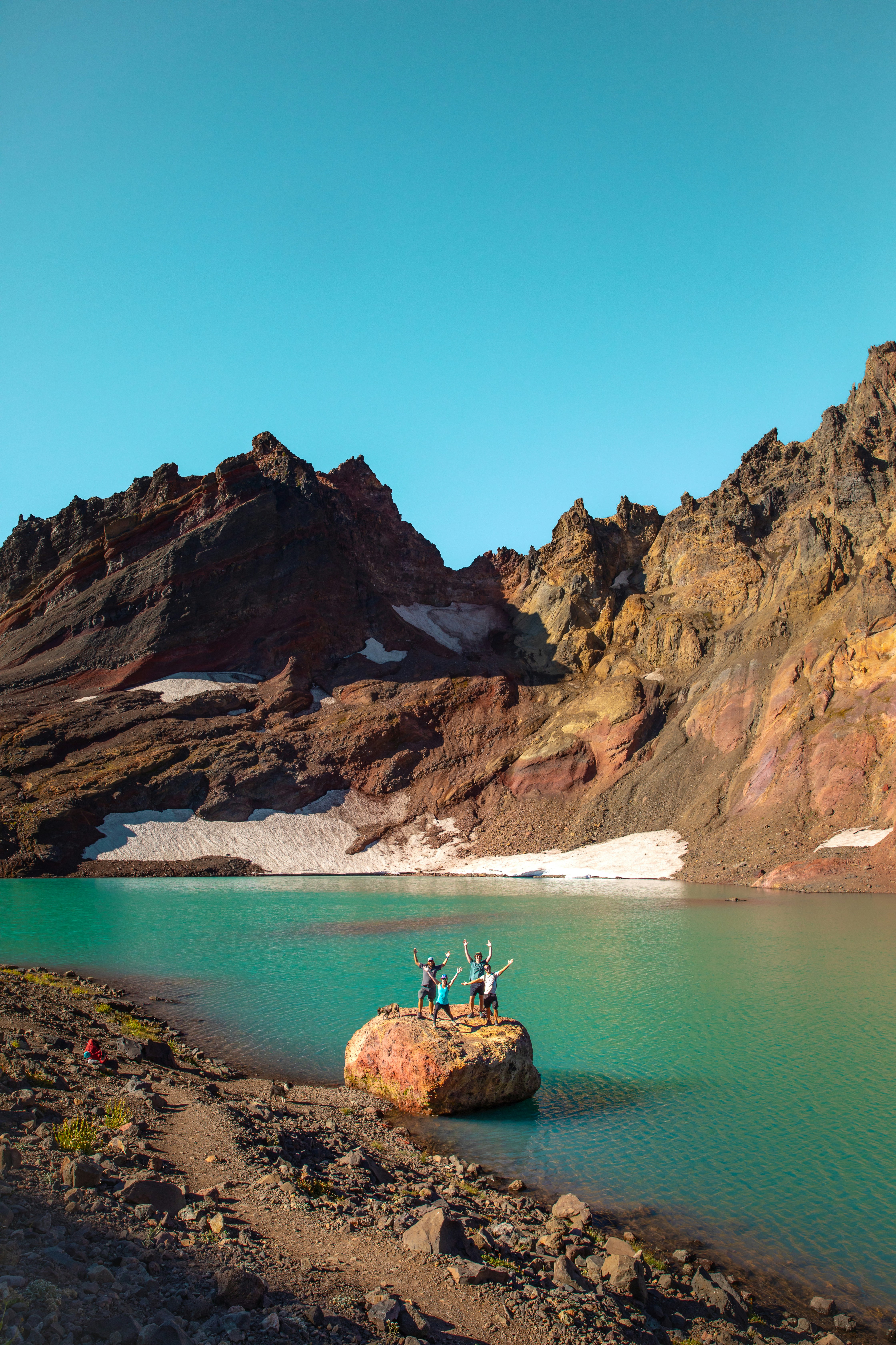 A couple of people standing on top of a rock near a lake